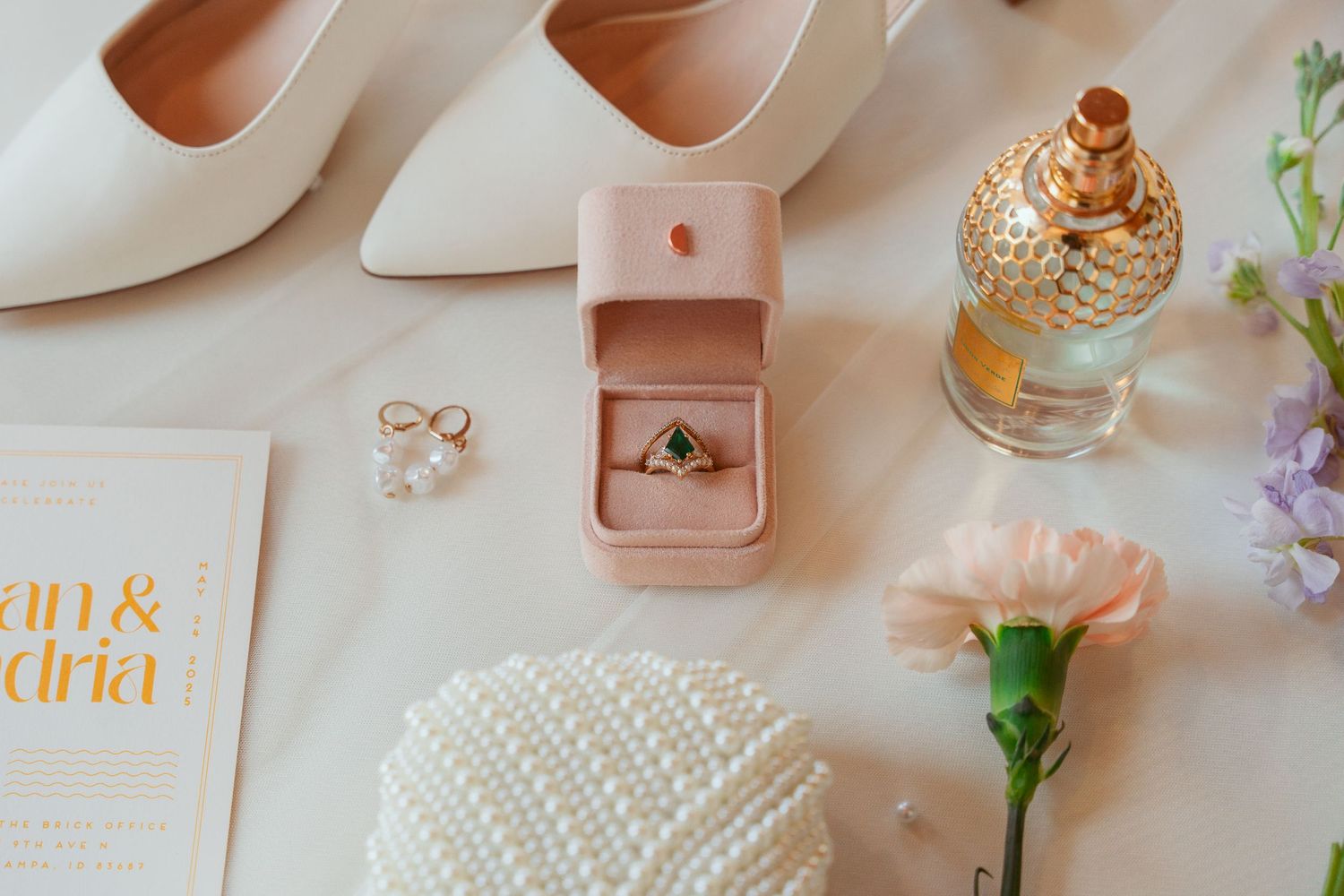 Wedding details including white heels, rings, perfume, and flowers arranged on a light surface.