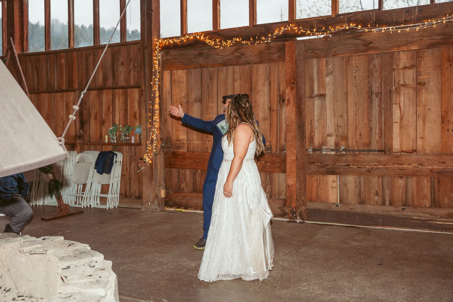 Dancers move across a wooden floor in a barn decorated with string lights and windows.
