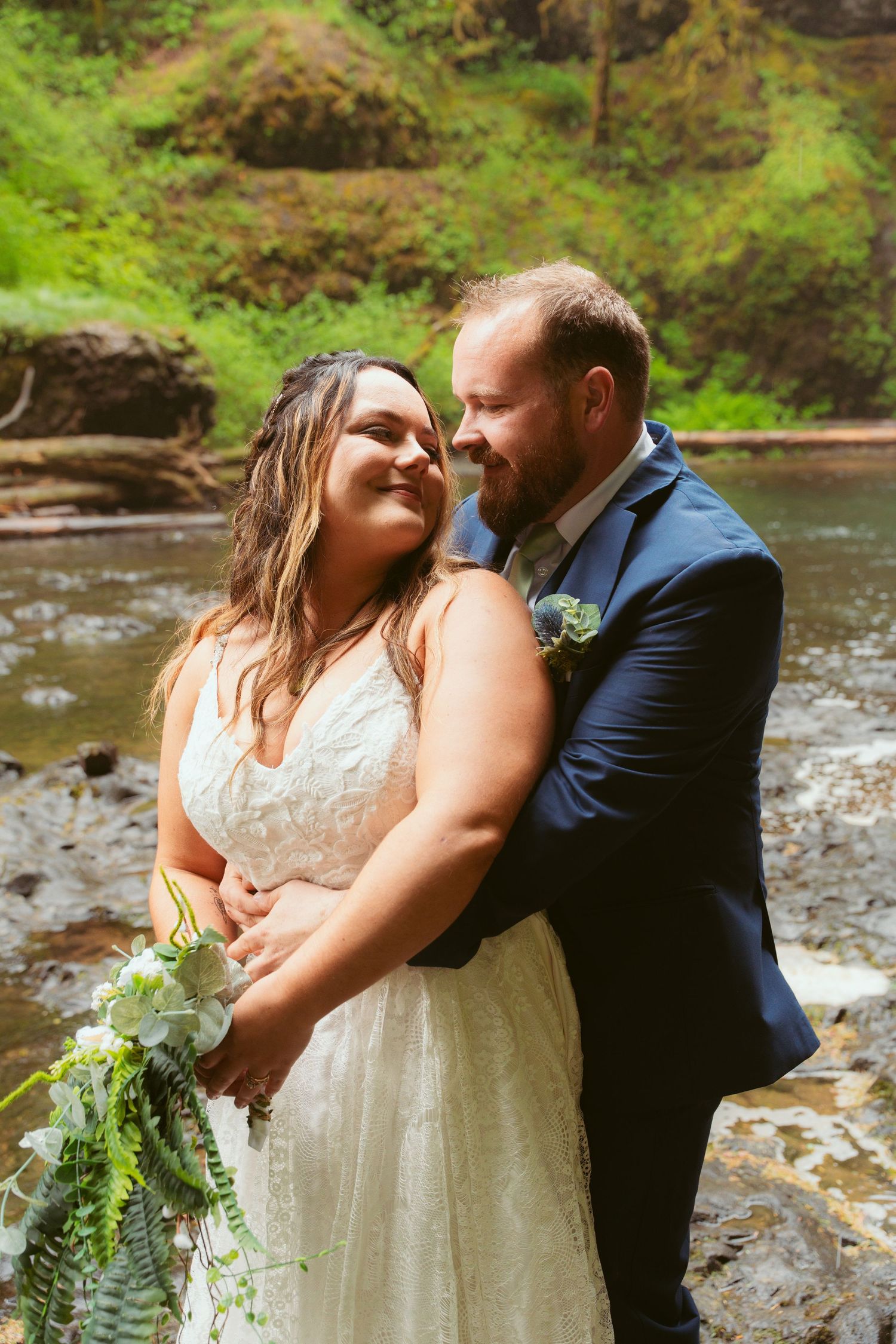 Romantic wedding portraits showing tender moments between newlyweds by a forest stream.