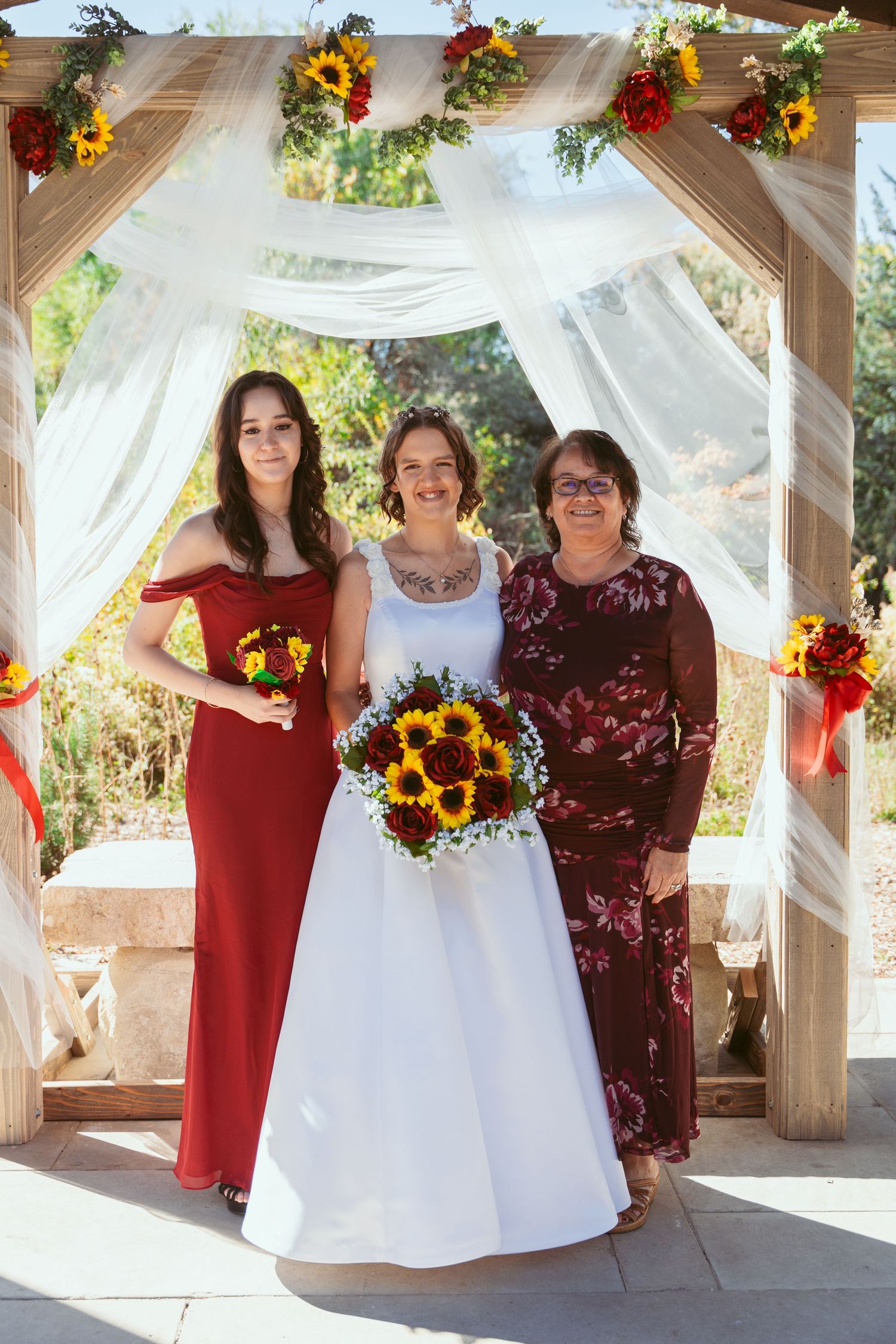 Wedding party gathers under covered pavilion decorated with white fabric and burgundy accents.