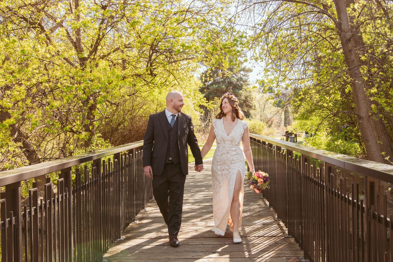 Wedding couple walking along a tree-lined wooden bridge pathway in autumn light.
