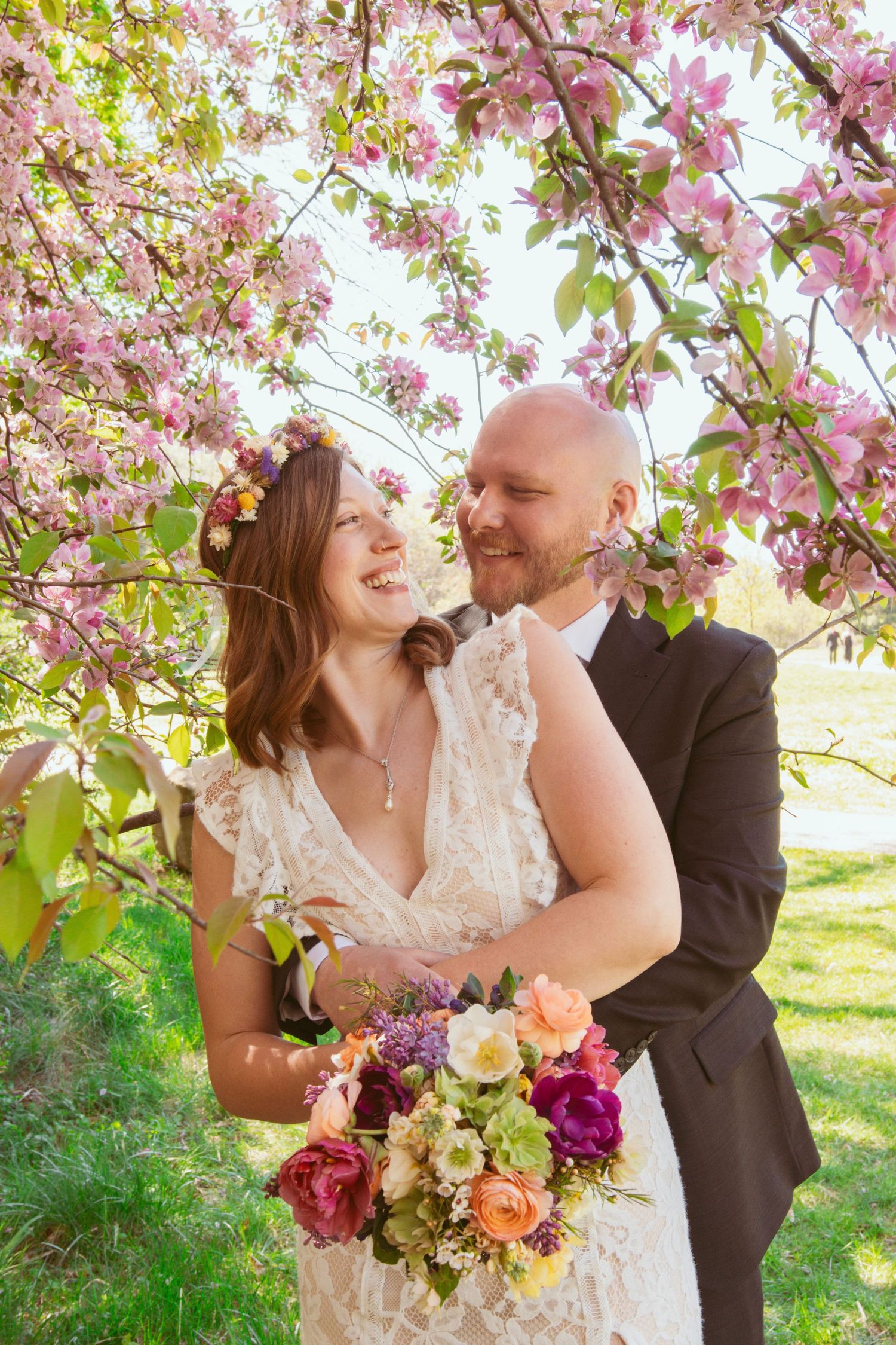 Couple embraces under blooming cherry blossom trees with colorful spring bouquet.