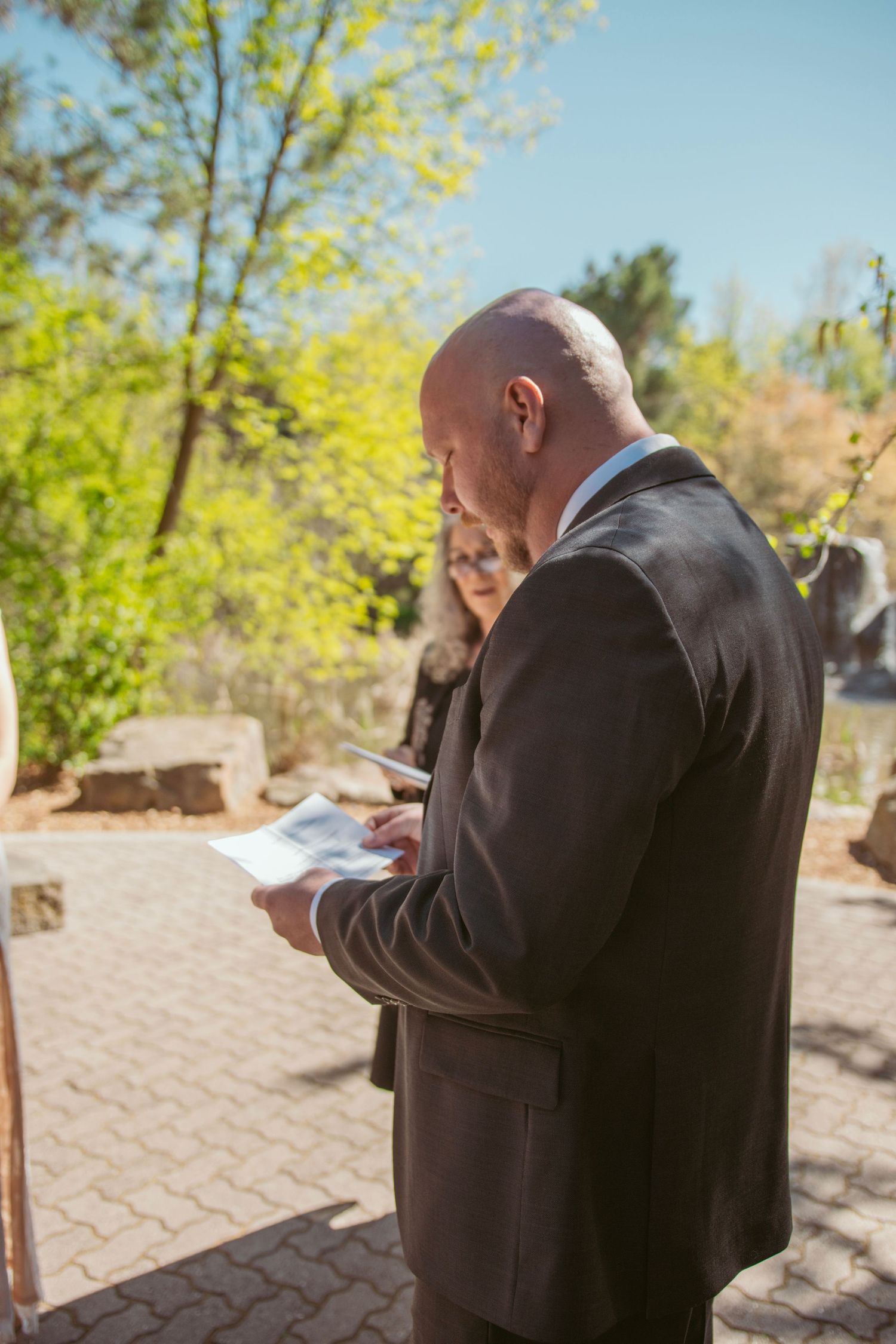 A wedding officiant reads ceremony notes outdoors on a sunny spring day.