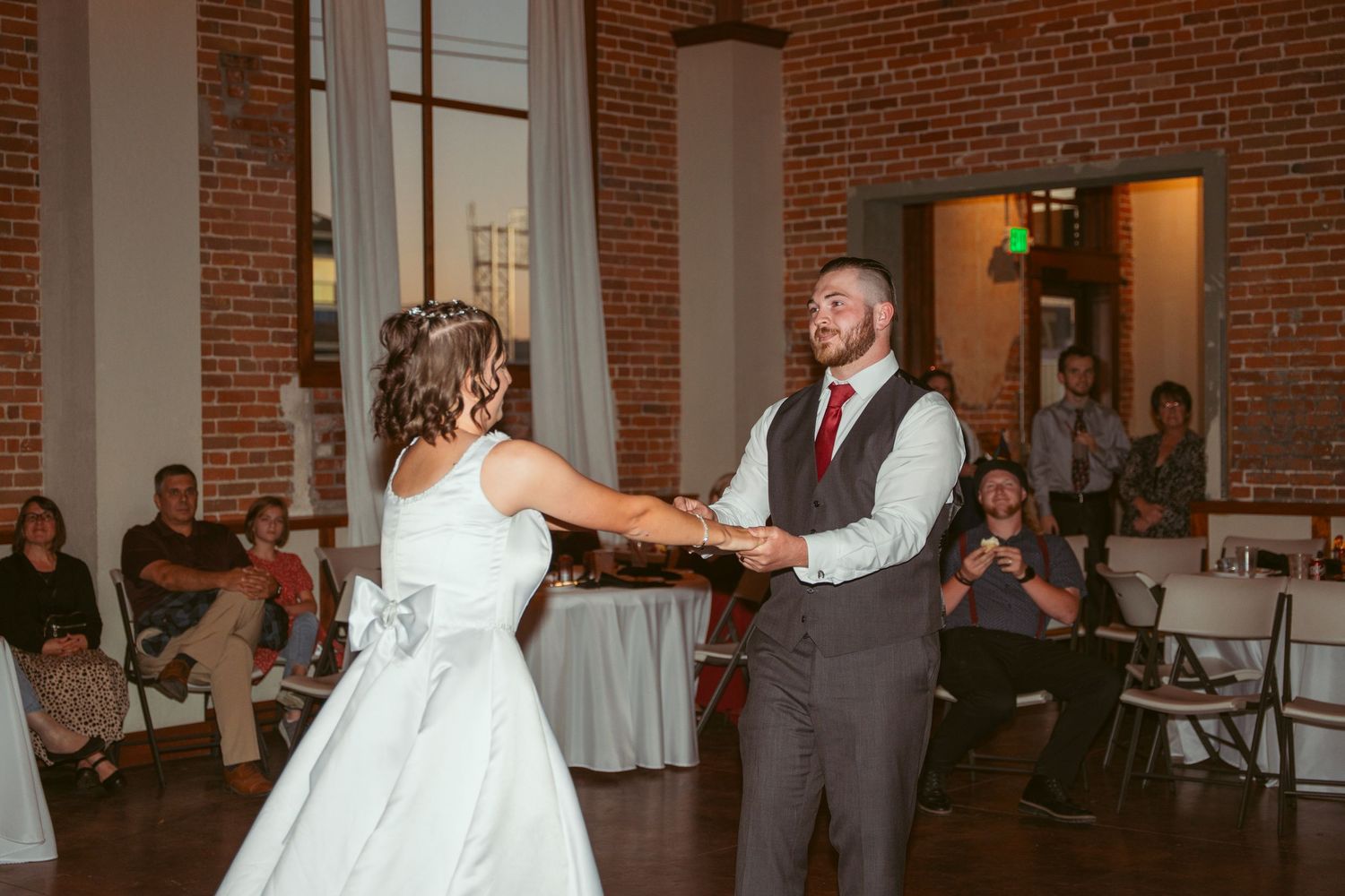 Wedding dance captured in a beautifully lit brick venue with guests watching from the sides.