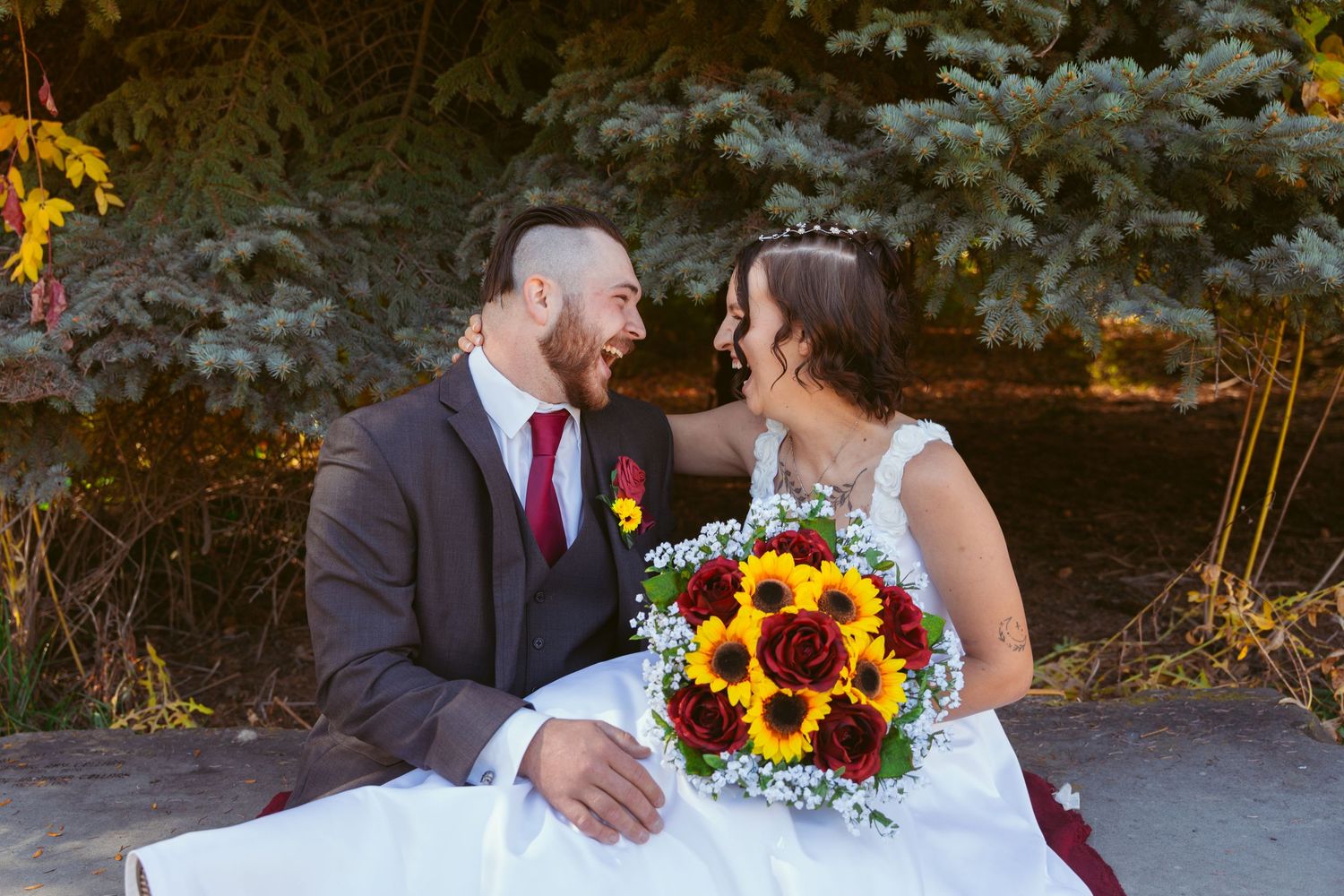 Couple shares intimate moment on stone bench with fall foliage in background.