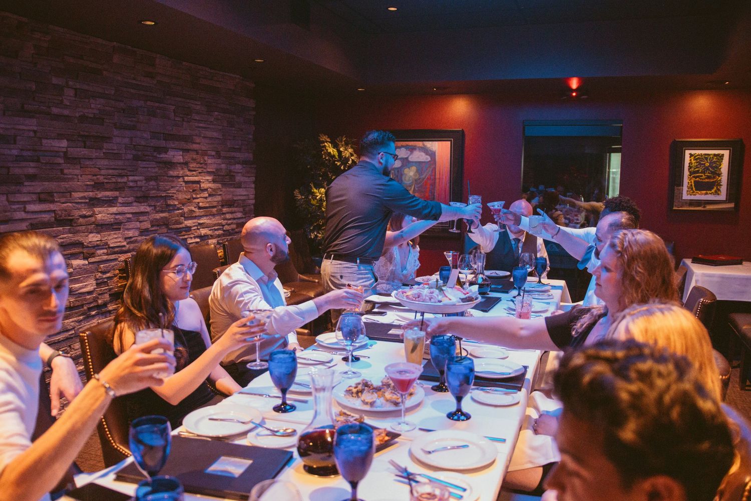 Wedding reception guests dine and celebrate in dimly lit restaurant with exposed brick walls.