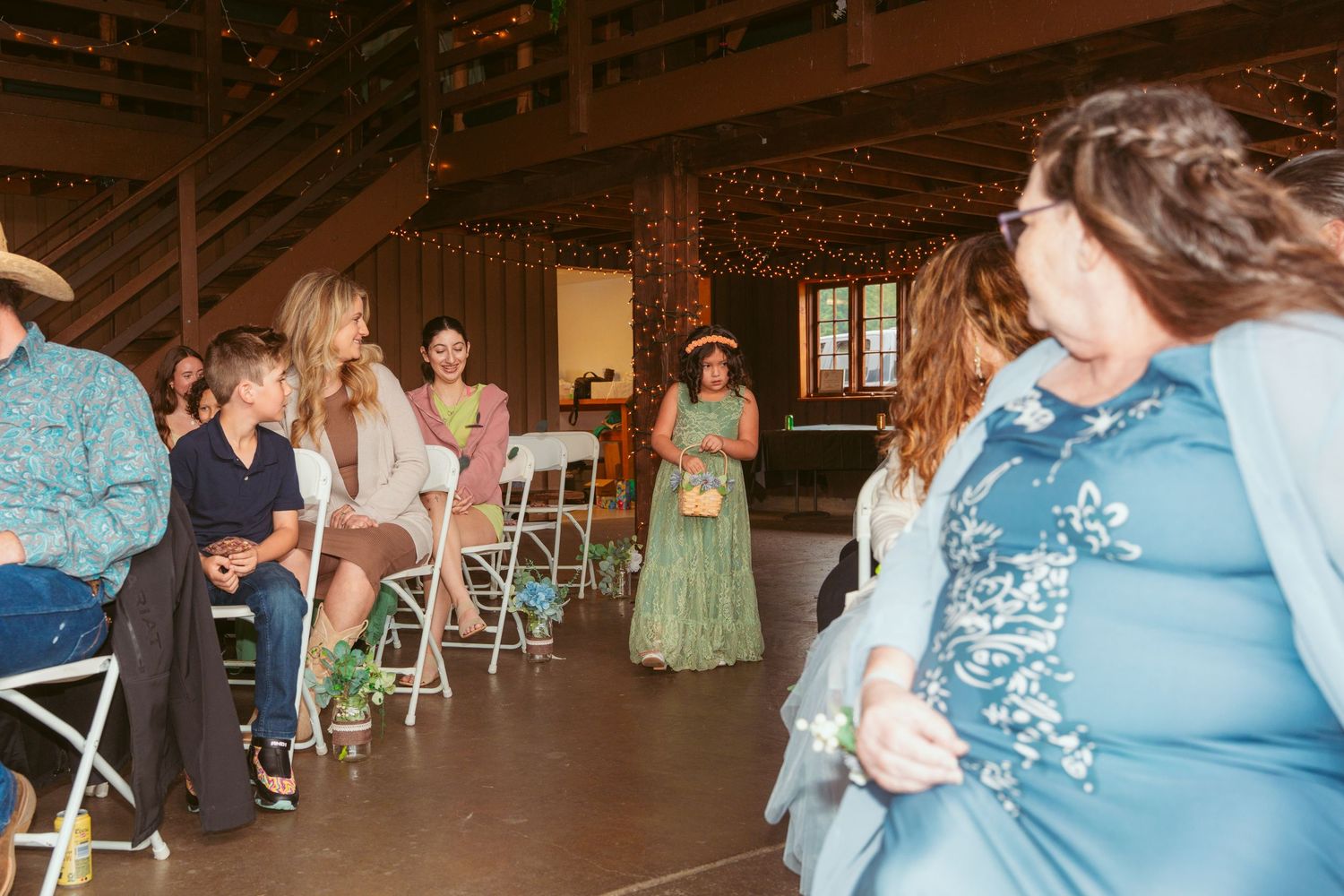 Rustic wedding reception with guests mingling under warm string lights in wooden barn.