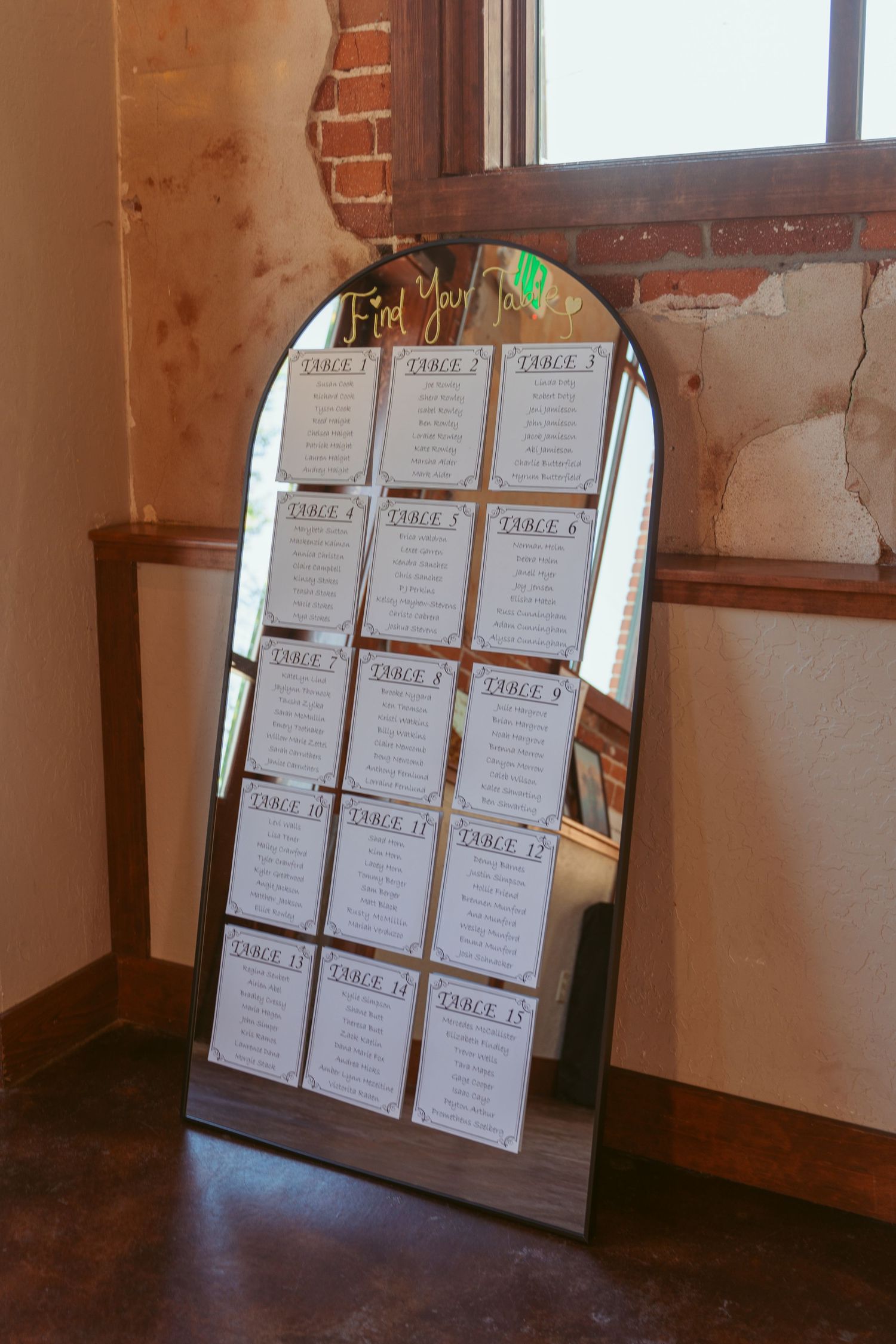 Wedding seating chart display with multiple tables arranged on mirrored panels in a rustic brick venue.
