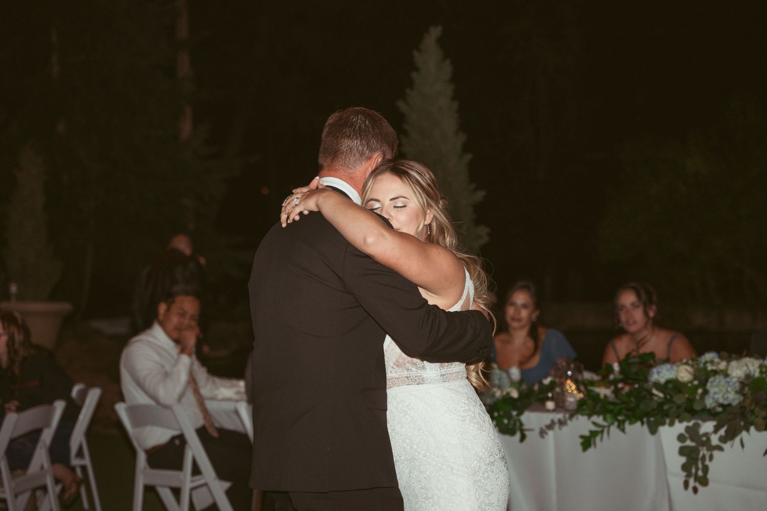 Wedding party celebrates on a dance floor decorated with overhead string lights and greenery.
