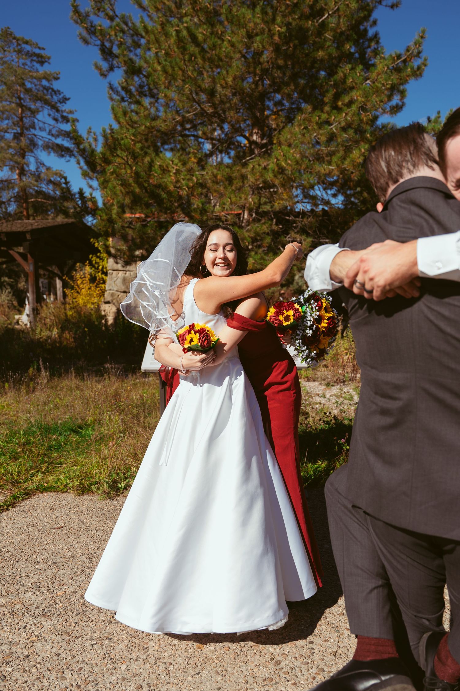 Wedding party members in burgundy and dark suits posing on a gravel path.