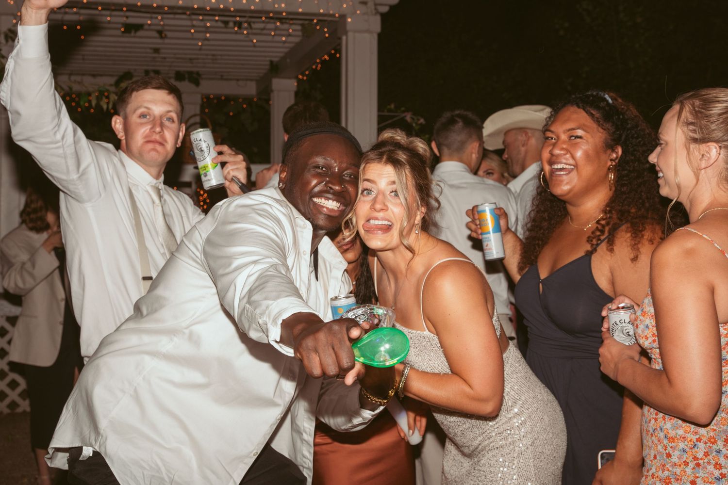 Wedding guests dancing and celebrating with drinks at a lively reception party.