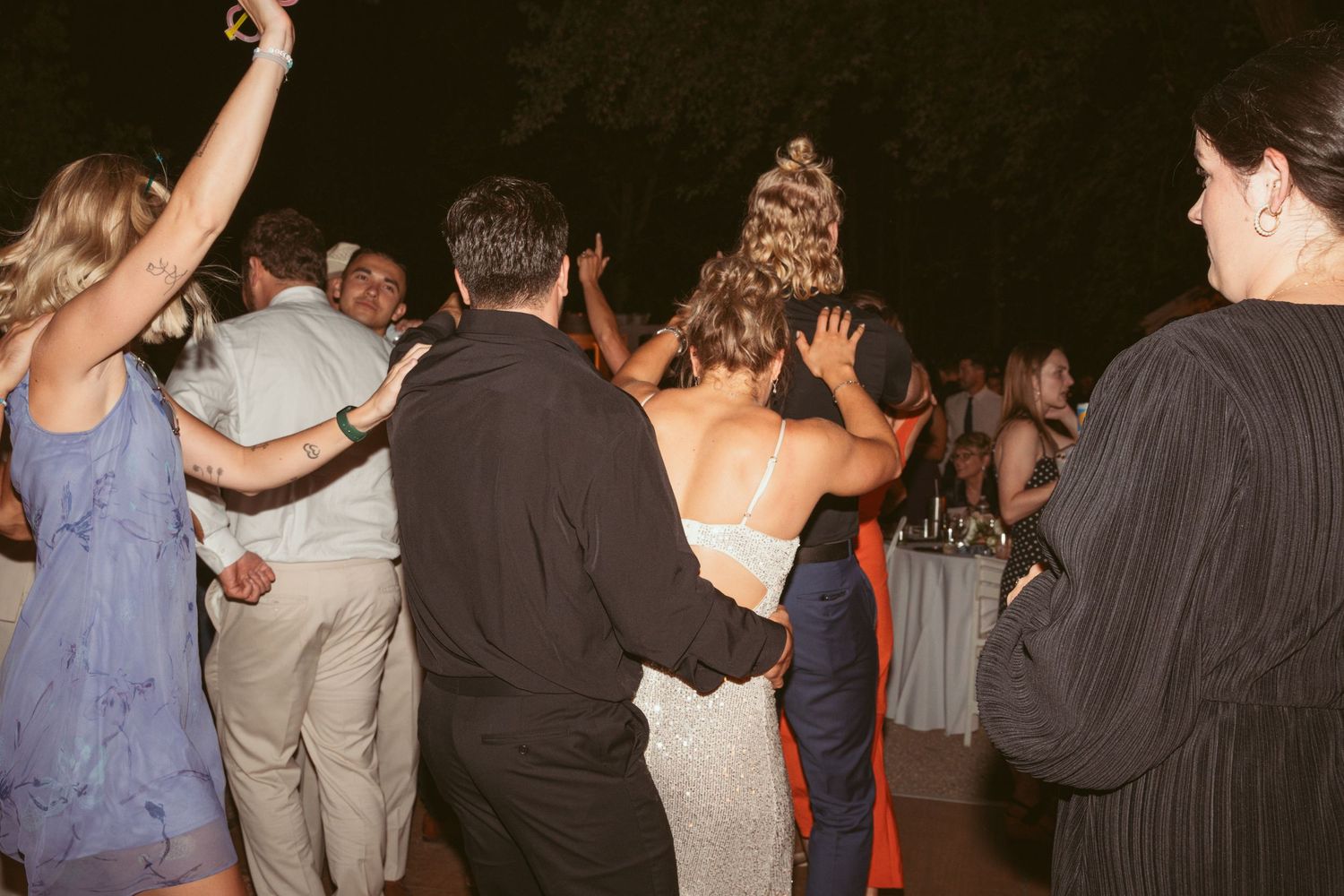 Wedding guests dancing together in a line formation during an evening reception celebration.