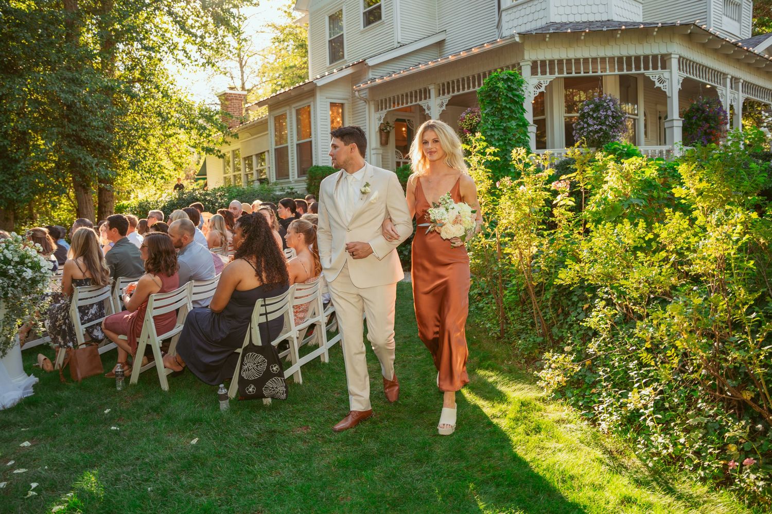 Outdoor wedding venue featuring white chairs and guests against backdrop of historic home.