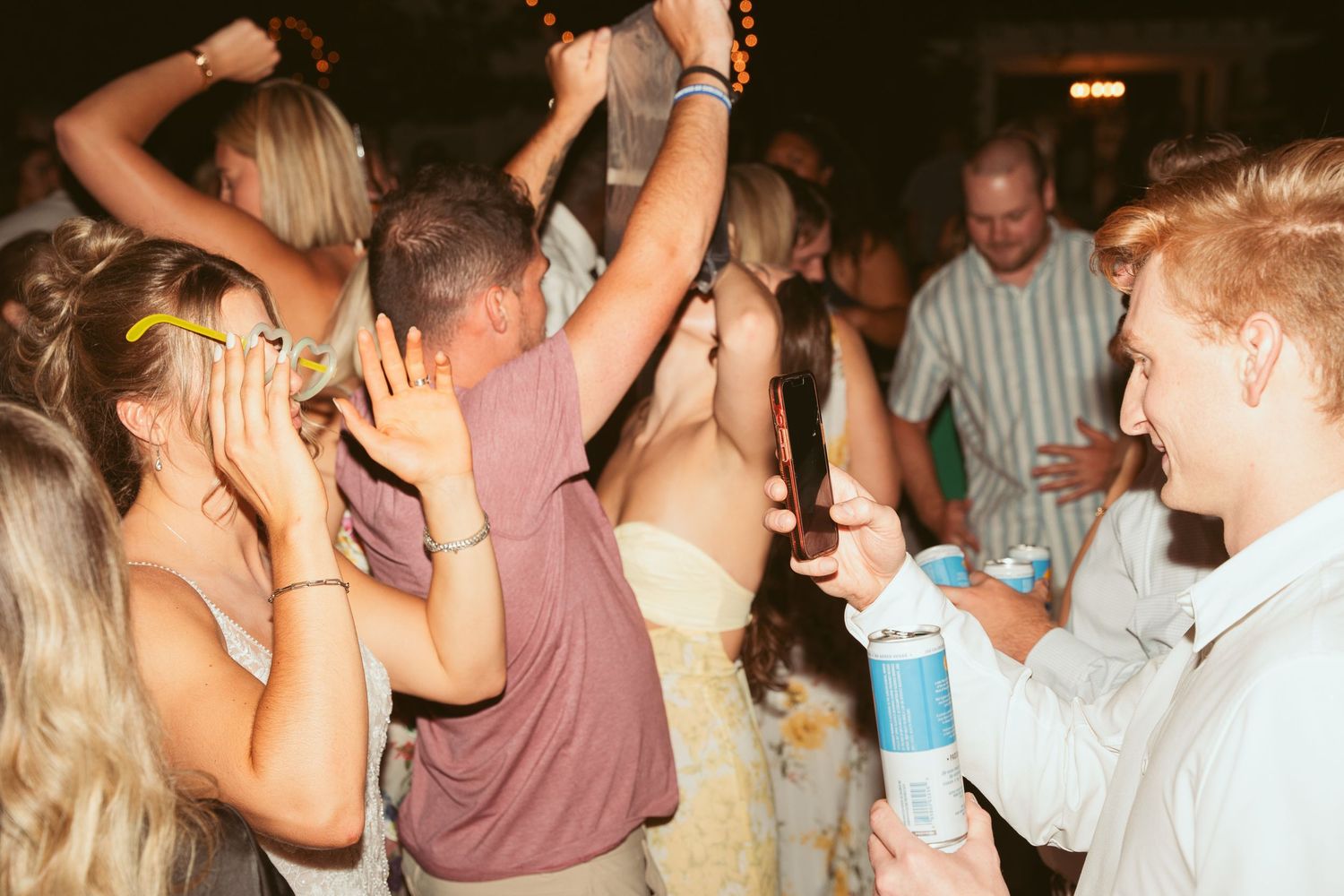 Energetic crowd dancing and celebrating with drinks at outdoor wedding reception.