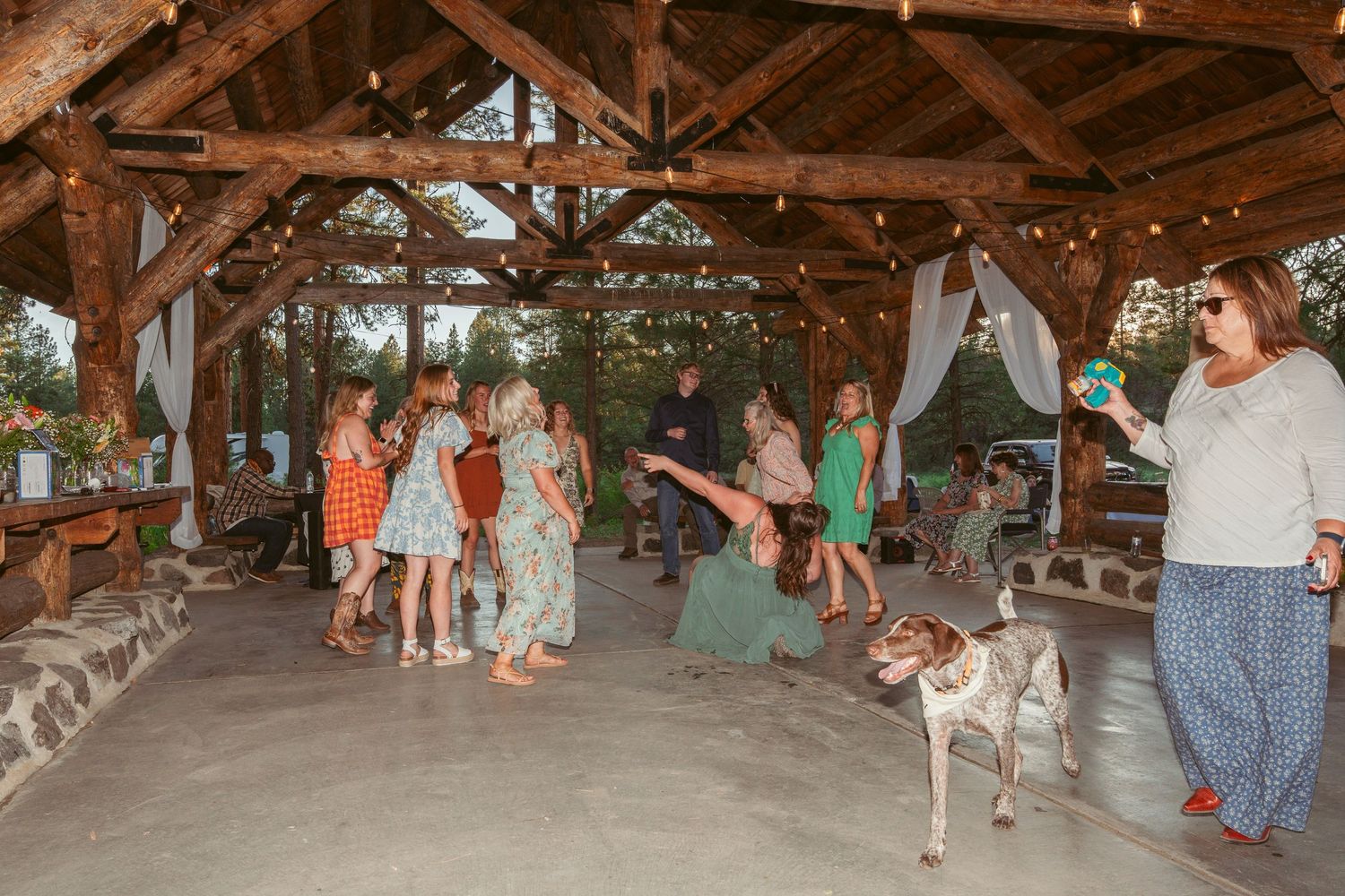 Wedding guests enjoying a dance party under a rustic wooden pavilion.