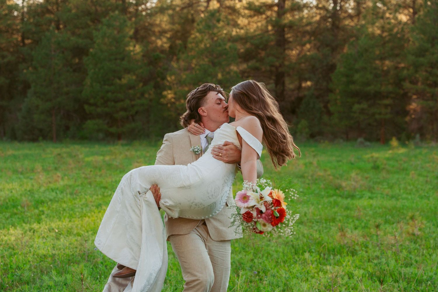 Romantic moments captured in a sunset meadow with evergreen forest backdrop.