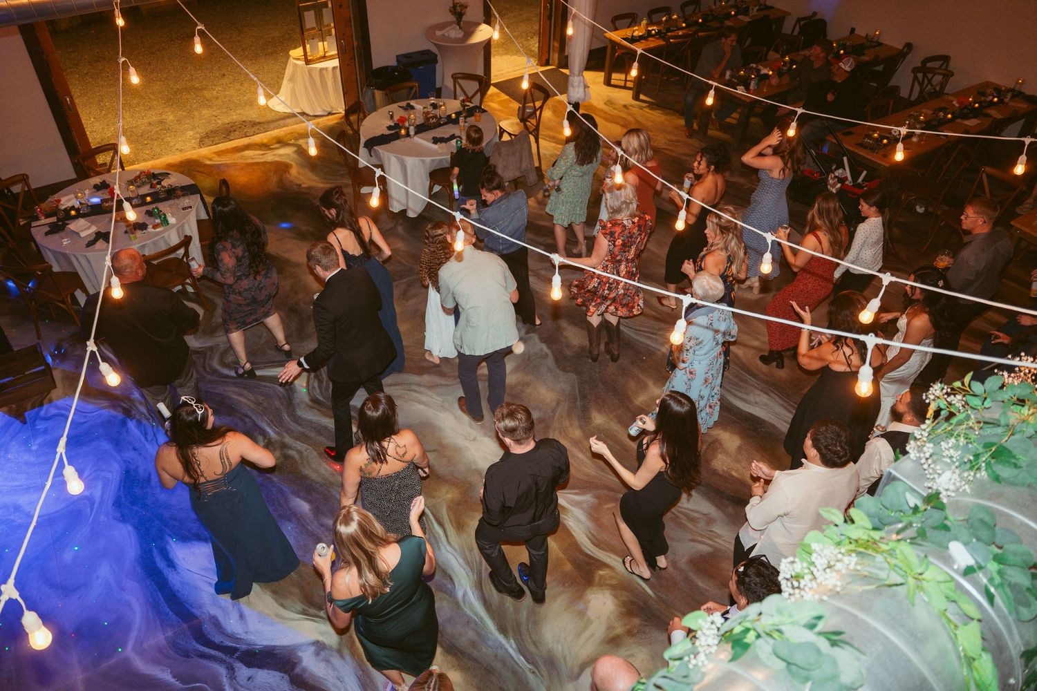 Crowded dance floor at night with colorful lighting and string lights overhead.