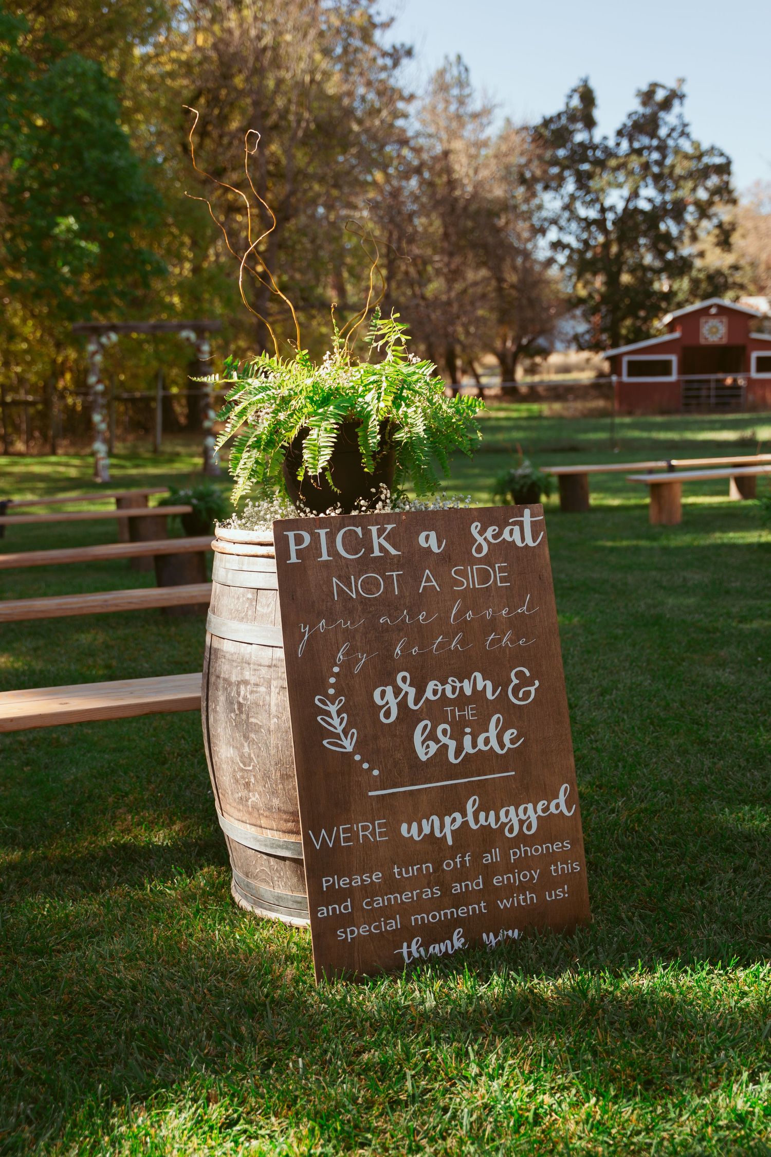 Rustic wedding sign on barrel reading Pick a seat not a side with greenery decoration.