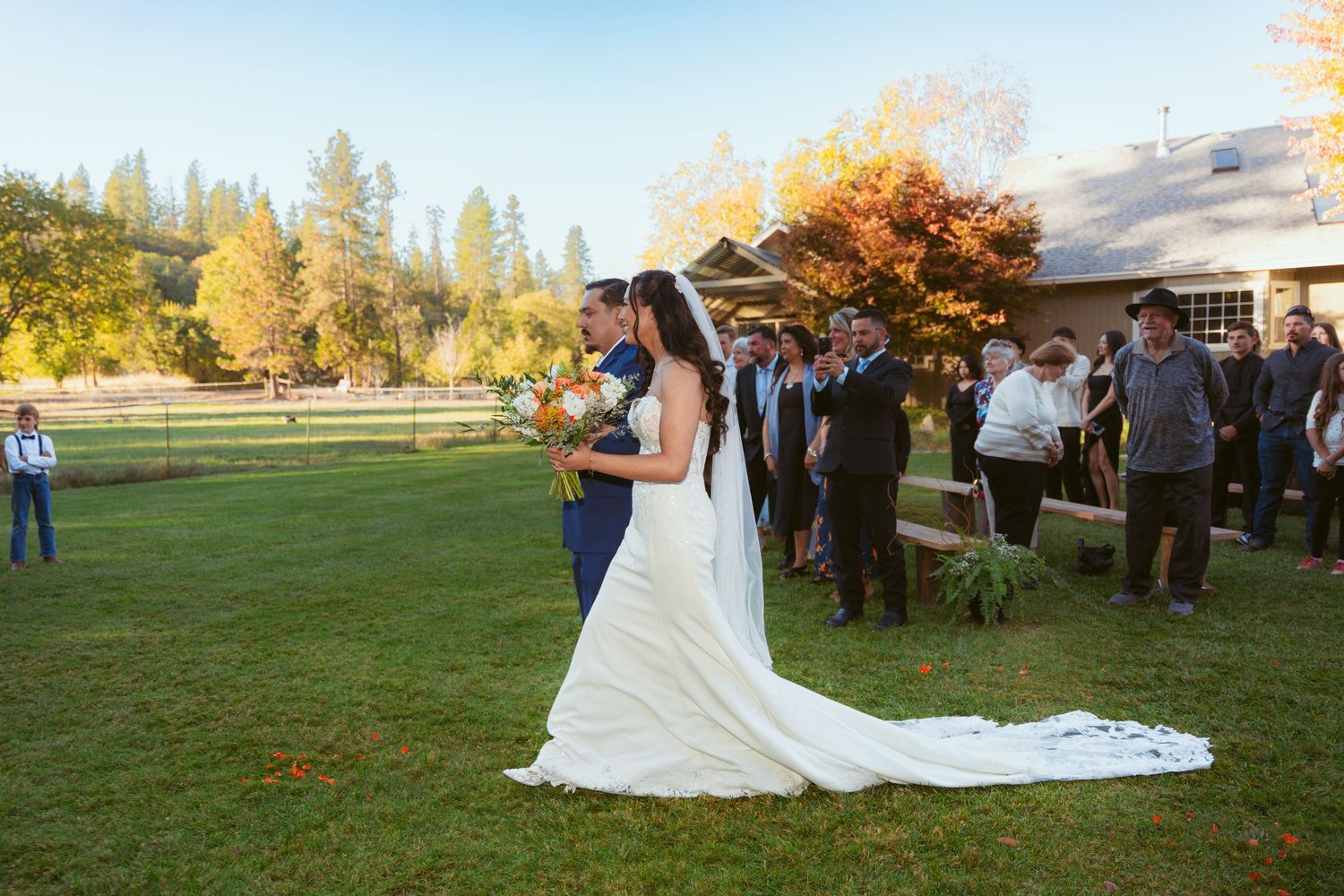 Wedding ceremony on lawn with fall colors and rustic barn setting.