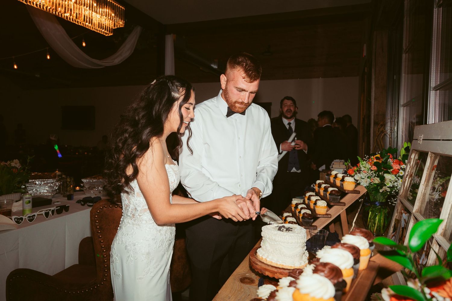 A couple shares a tender moment while cutting their wedding cake together at their reception celebration.