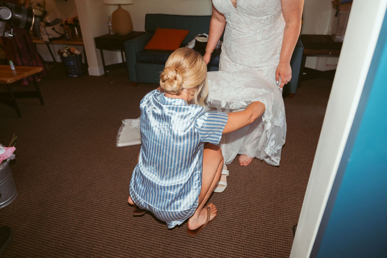 Final wedding dress adjustments being made in a carpeted room with blue walls.