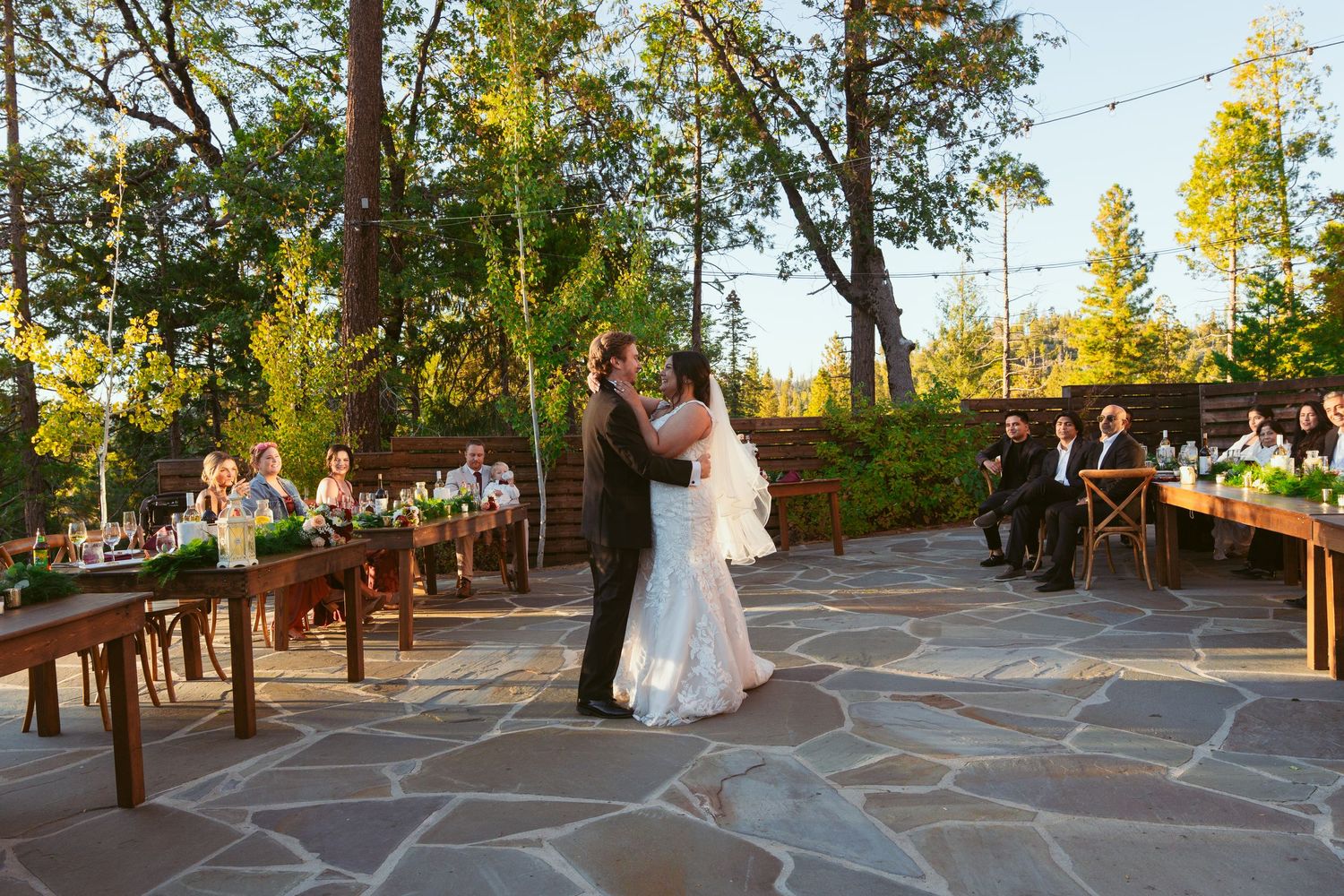Wedding party celebrates on rustic stone patio surrounded by wooden fencing and natural scenery.