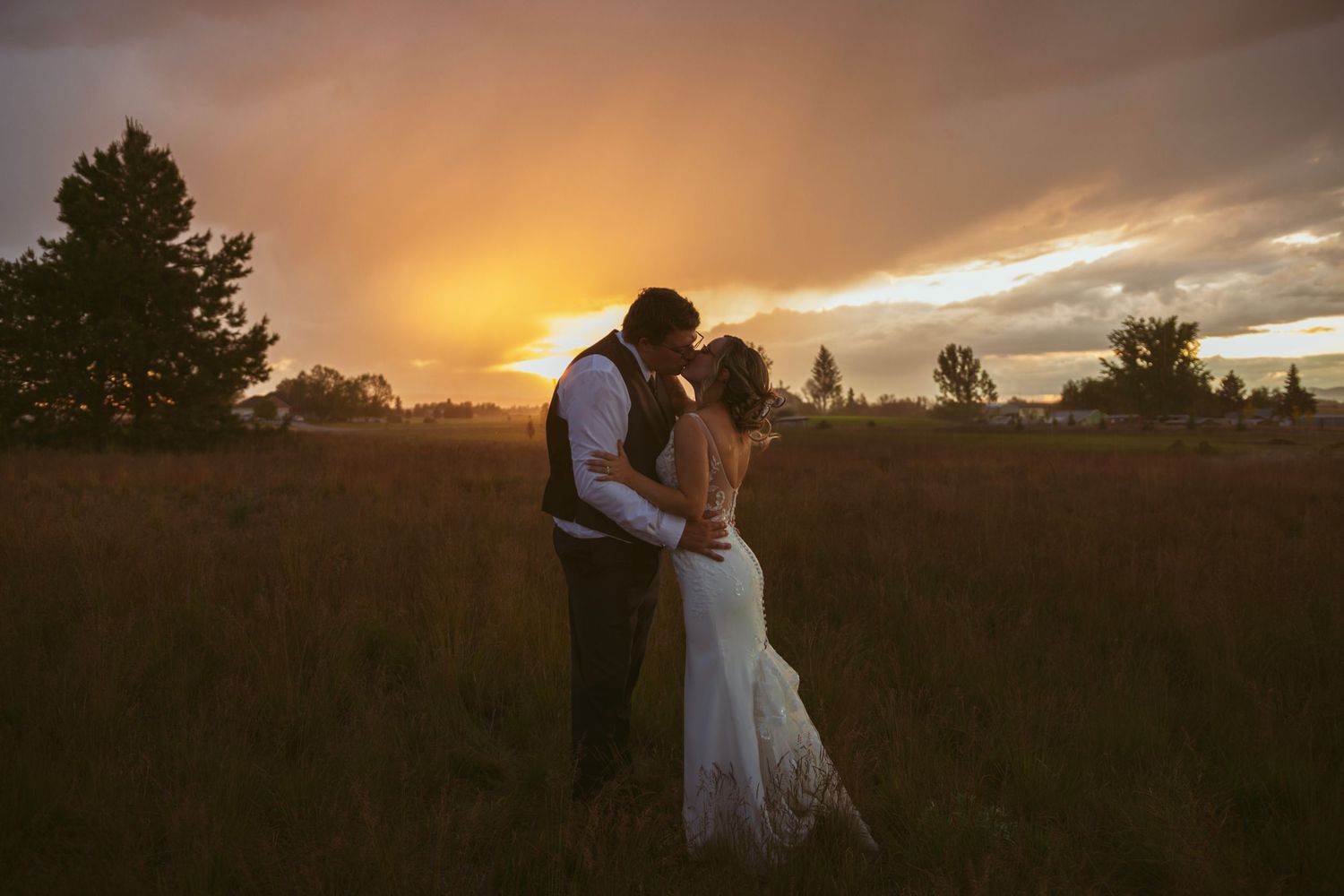 A couple embraces in a field bathed in warm sunset light during their wedding celebration.