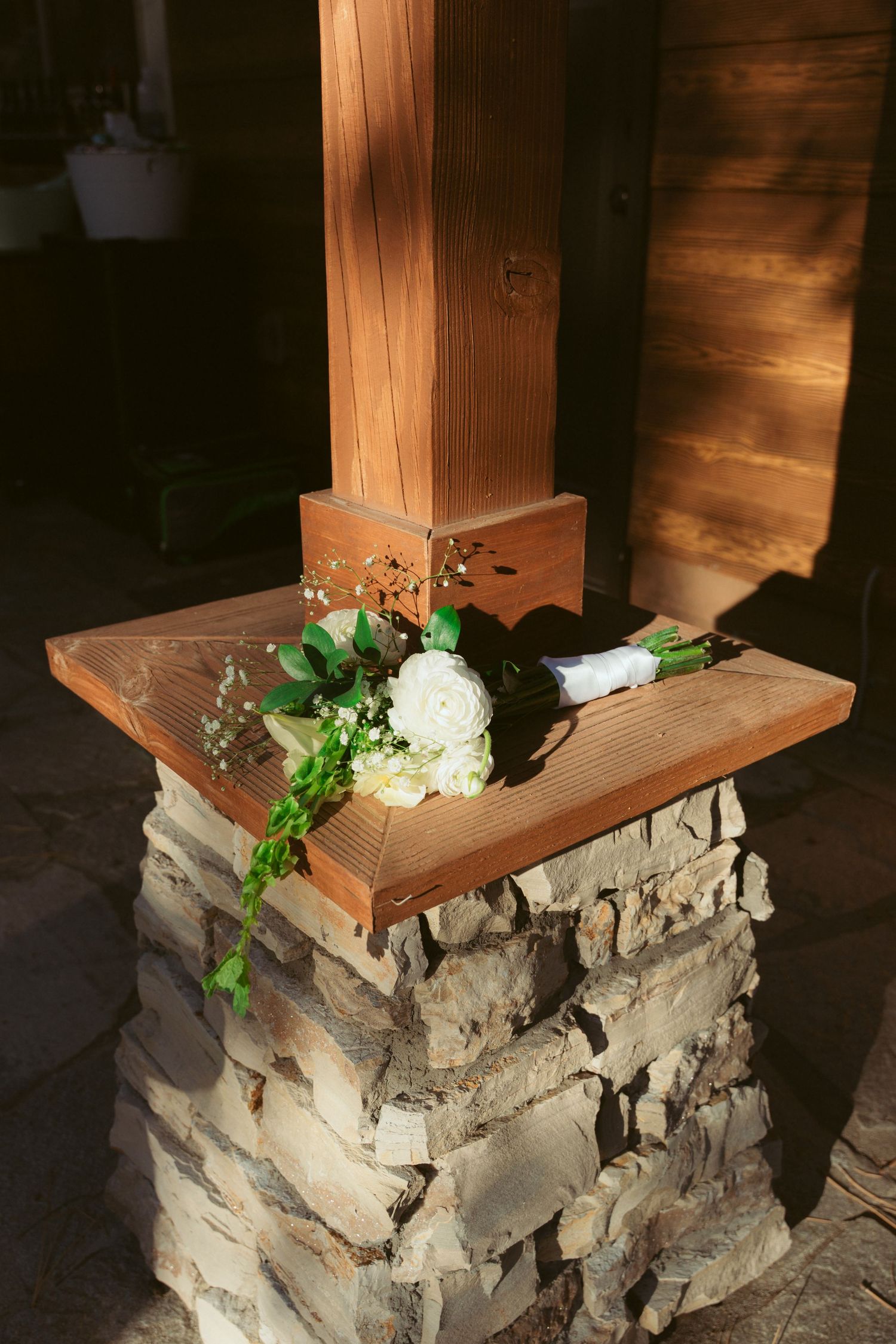 Stone and wood pillar display stand decorated with white flowers and greenery.