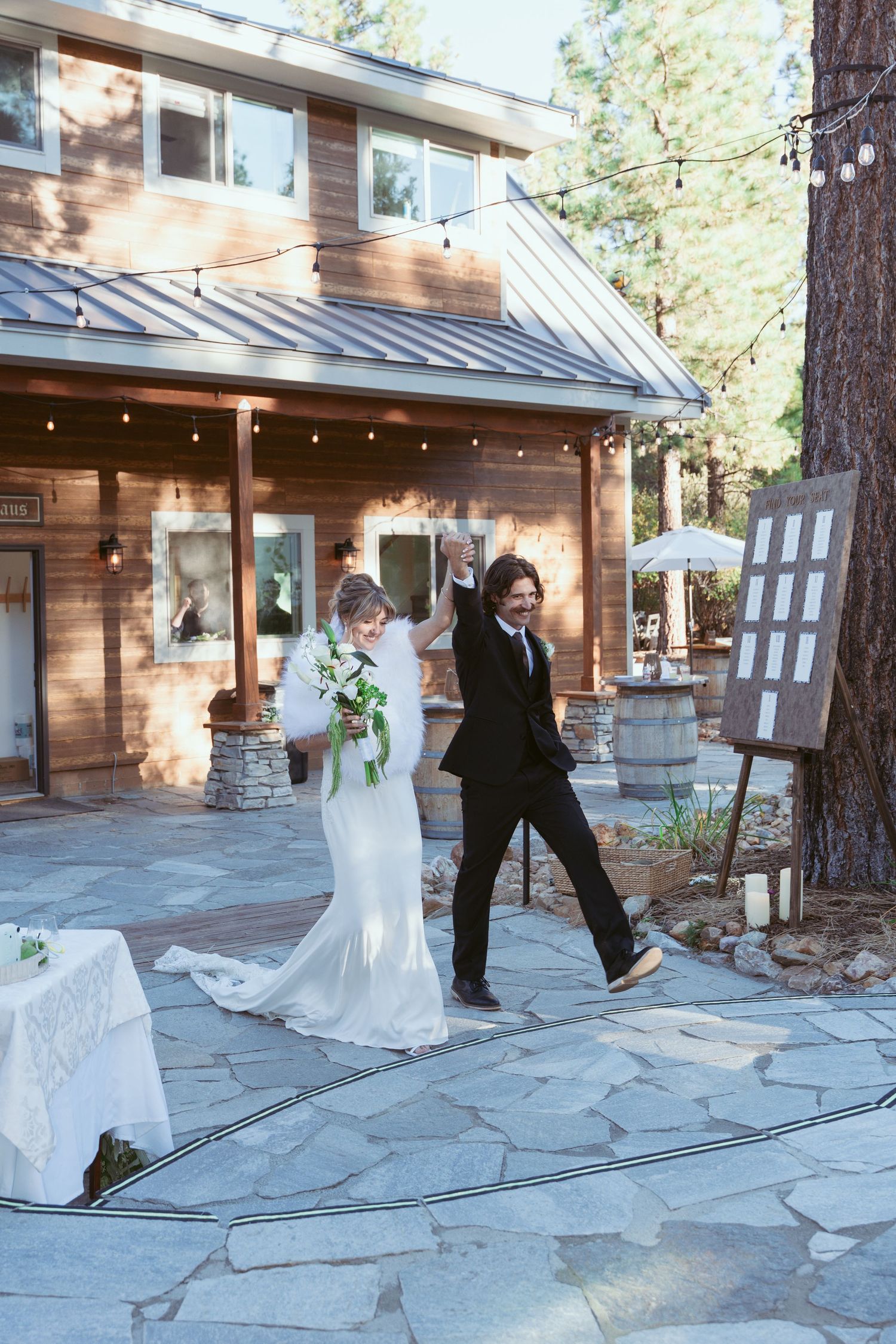 Wedding party walking outside rustic lodge with stone pathway and pine trees.