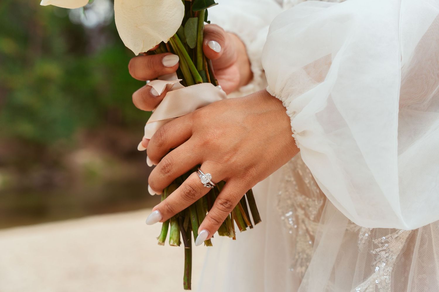 Close-up of bride's hands holding white floral bouquet with engagement ring visible.