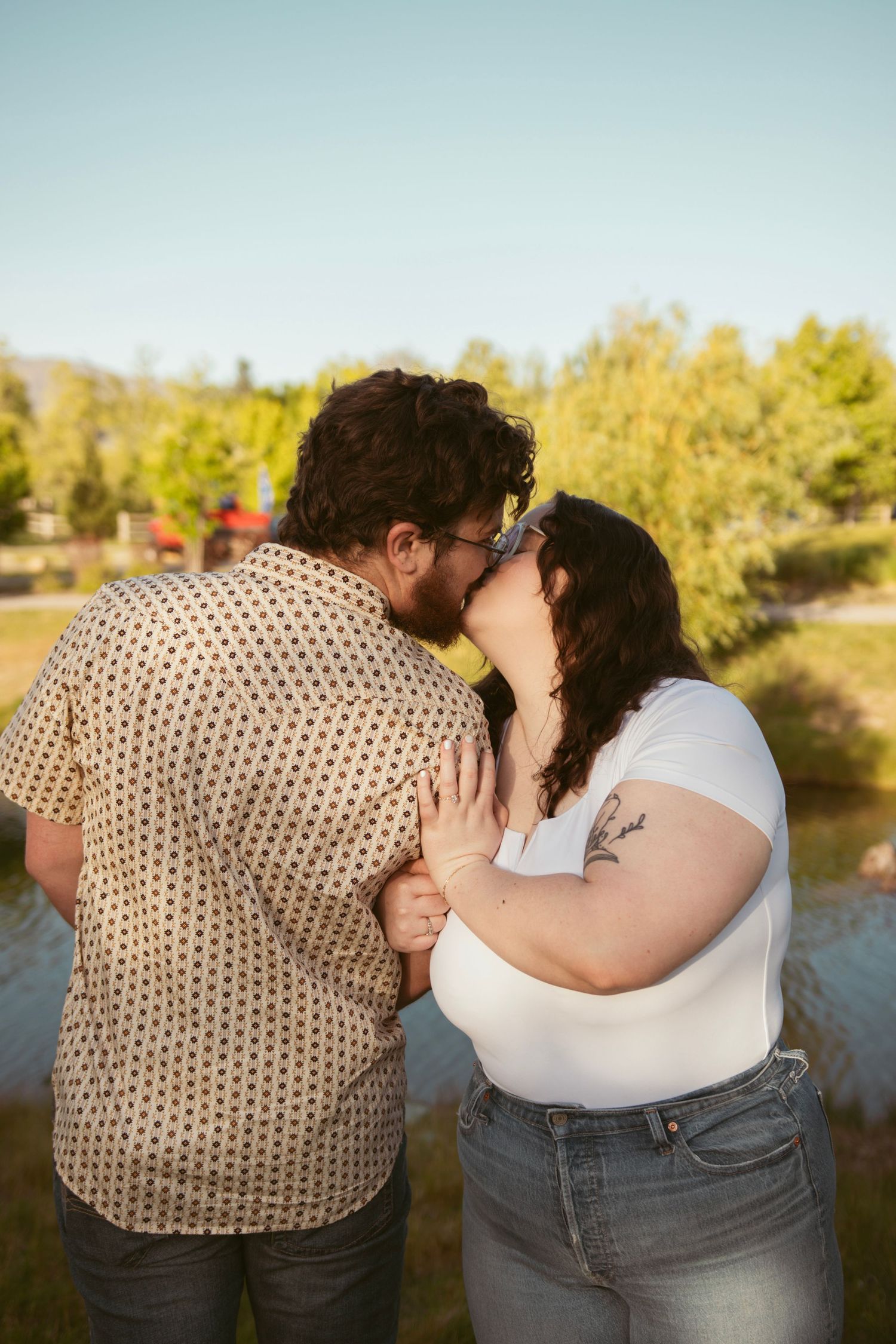 A couple shares a kiss on a deck with autumn trees in the background.
