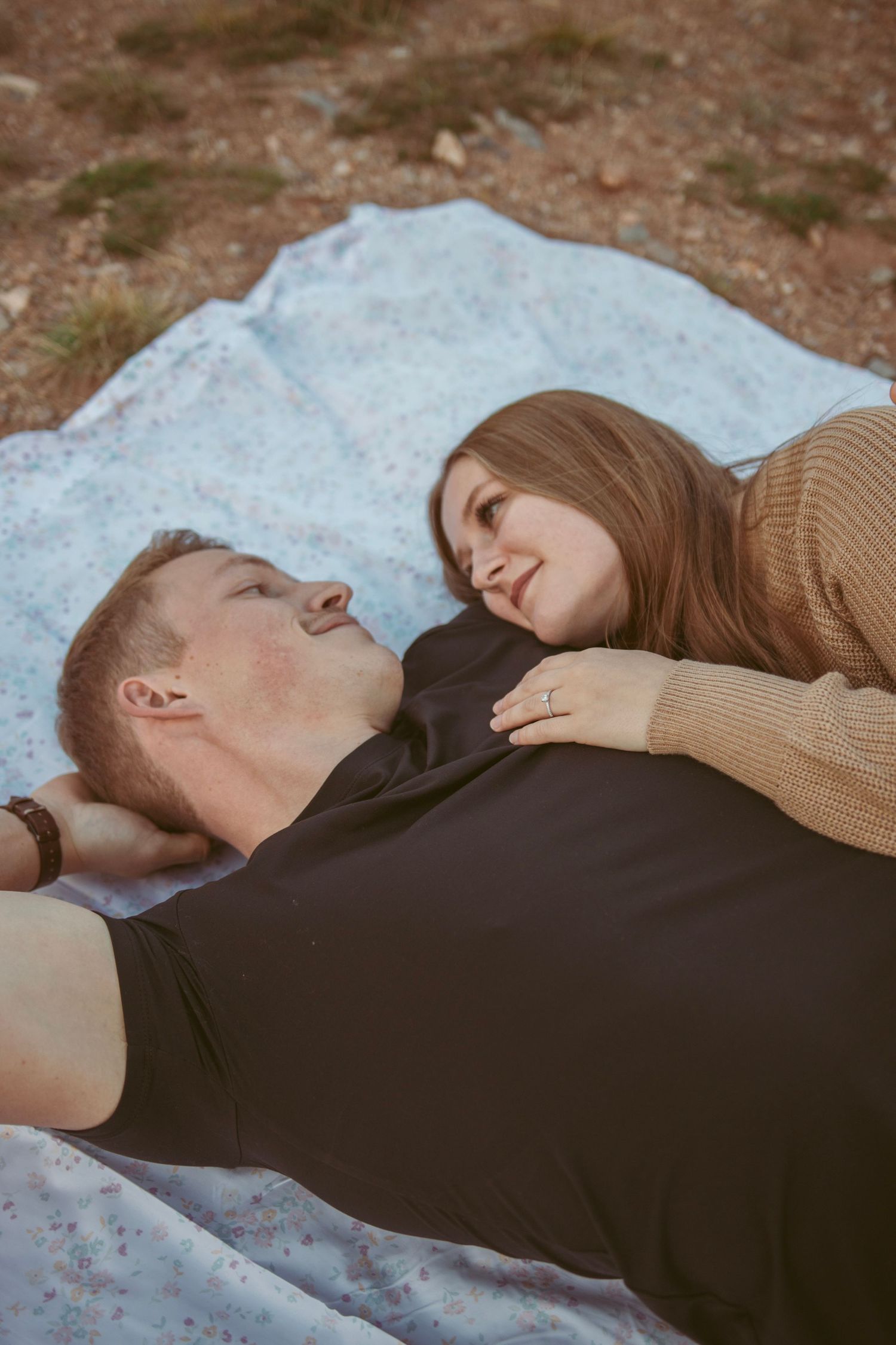 Close up of couple laying on light blue blanket against rocky mountain backdrop.