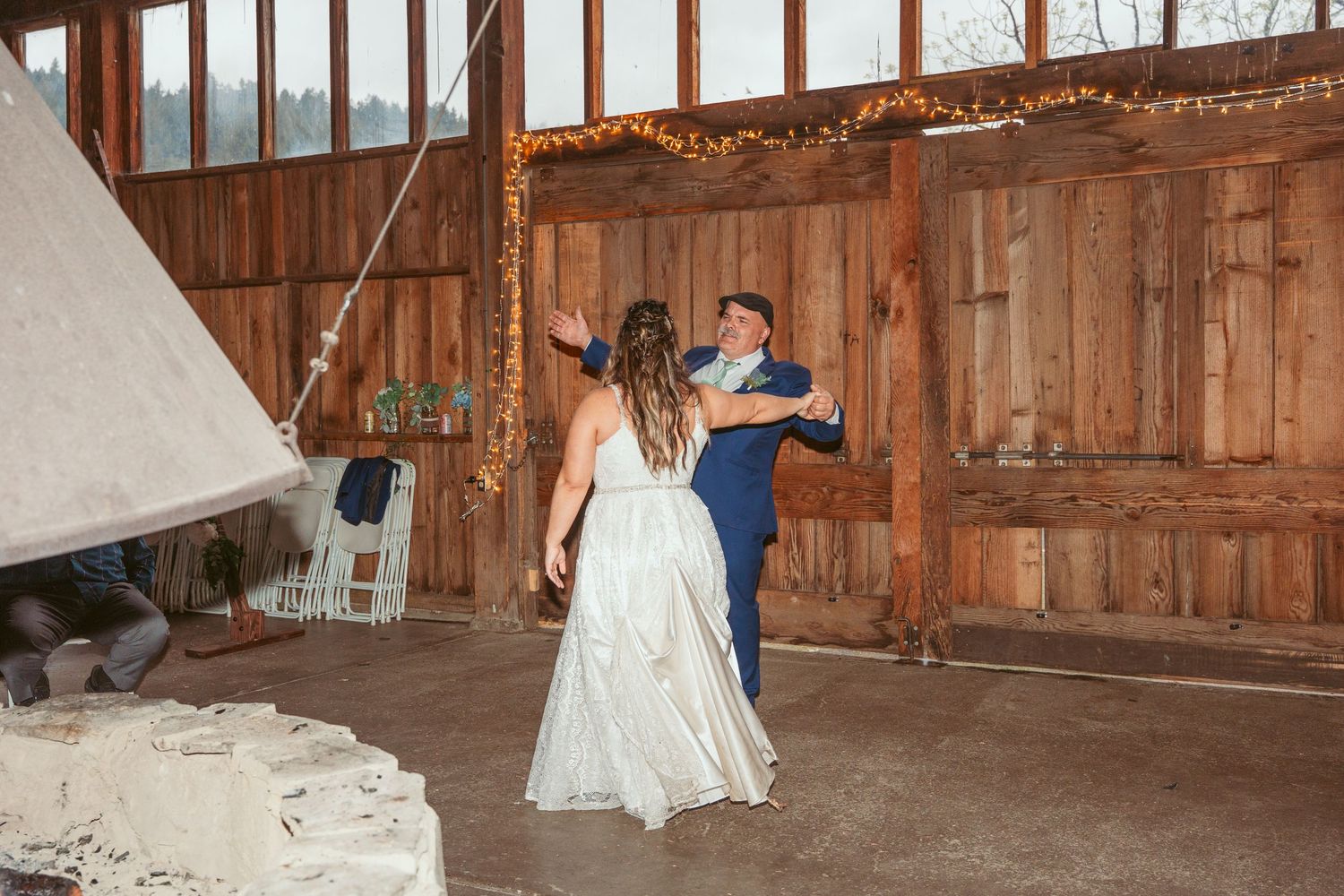 A couple dances in a rustic wooden barn with natural light streaming through windows.