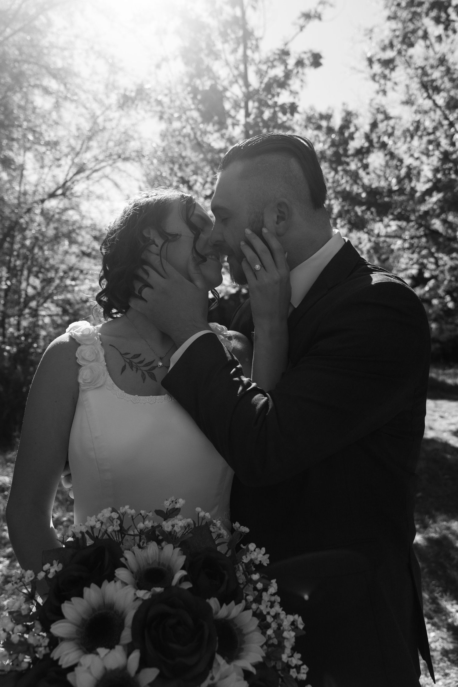 A black and white wedding photo capturing an intimate kiss with sunflowers in the foreground.