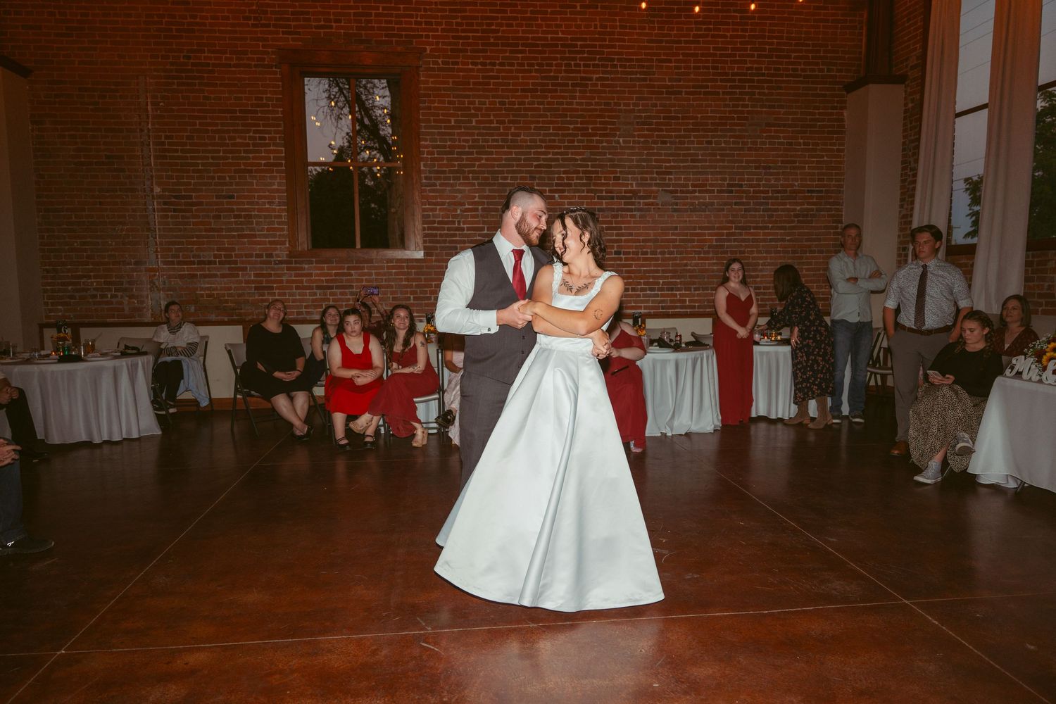 Couples dancing at wedding reception in rustic brick-walled venue with string lights.