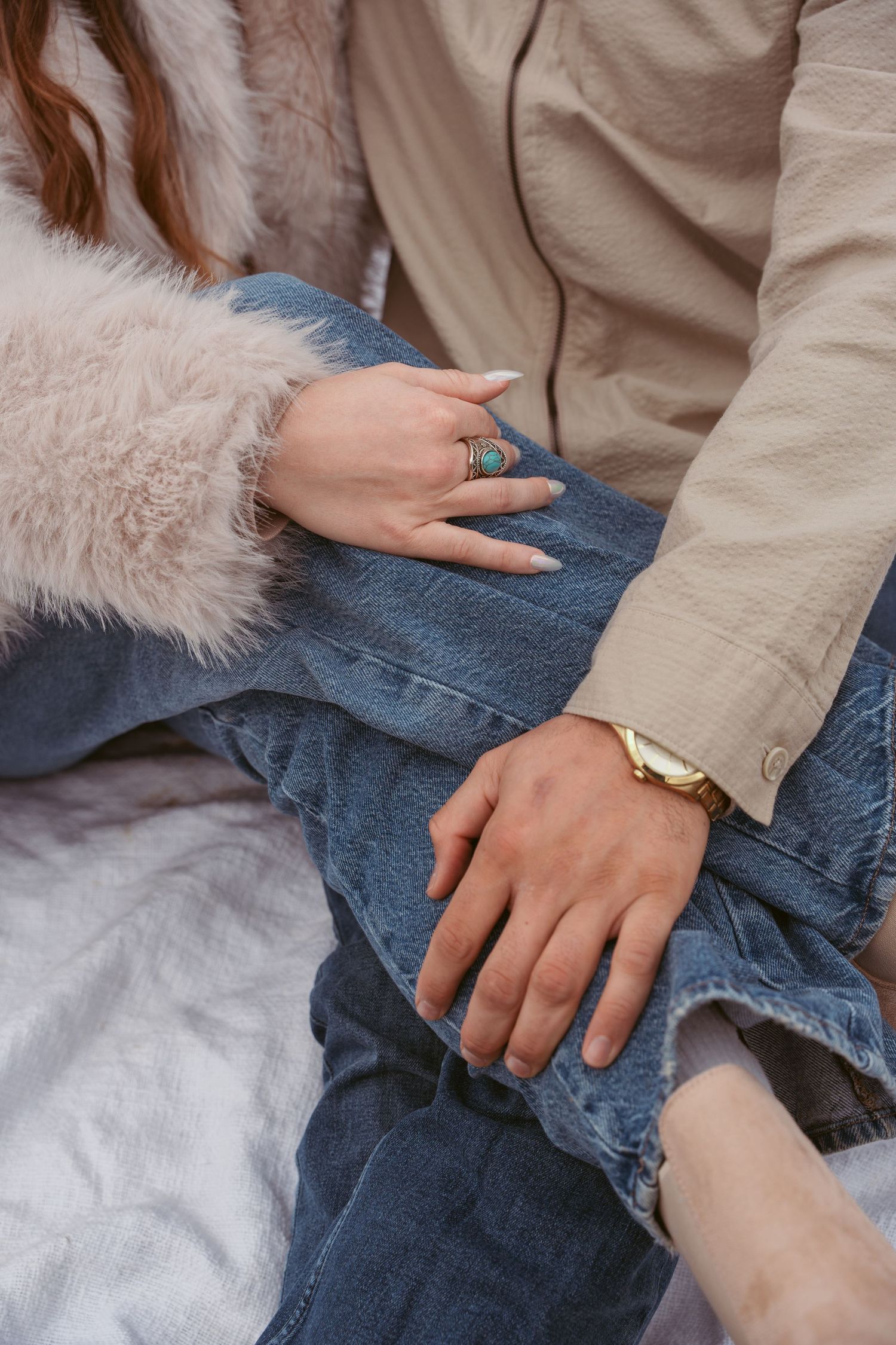 Close-up details of hands and denim during intimate couple photoshoot on white blanket.
