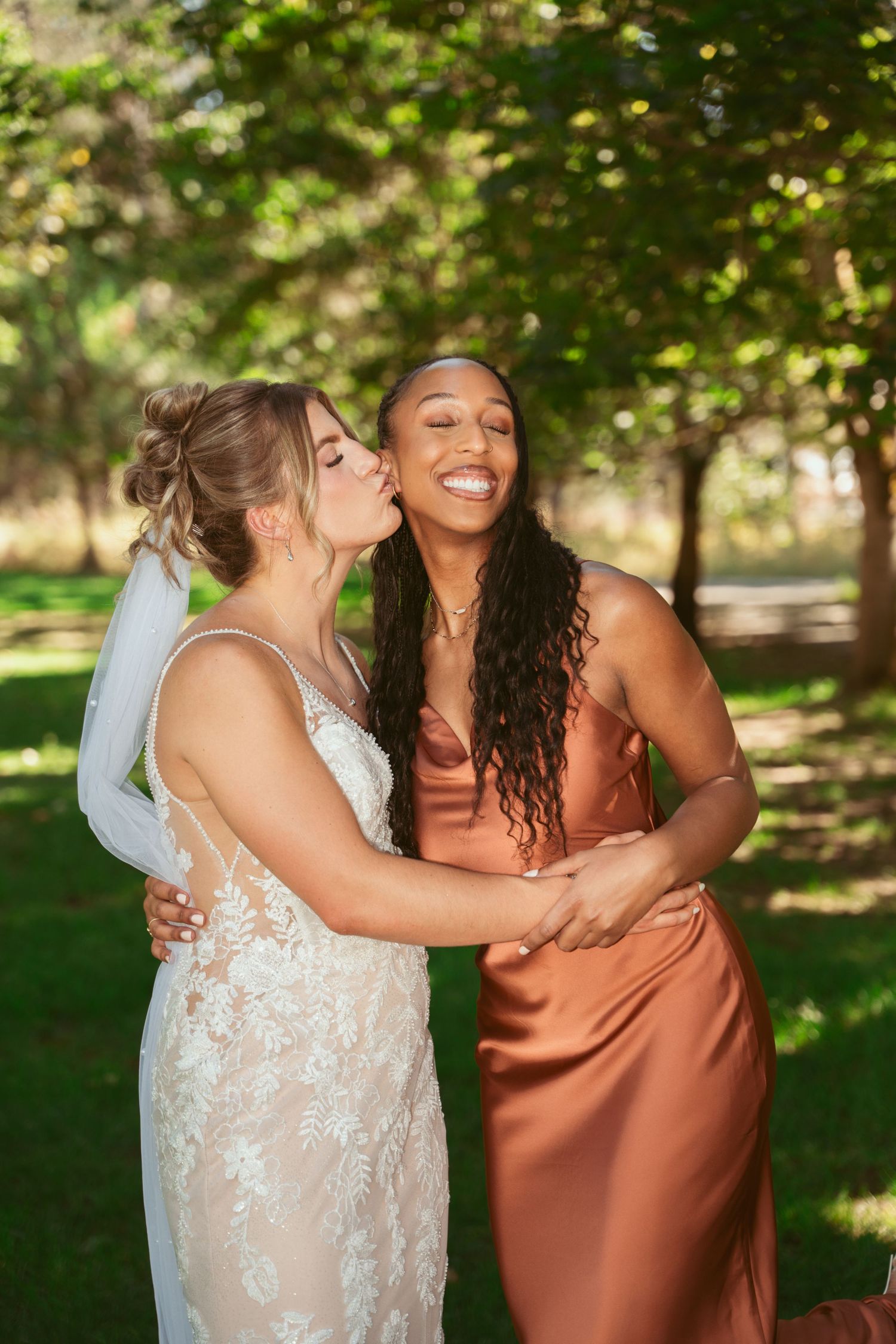 Wedding party members sharing joyful moments in a sunny outdoor garden setting.