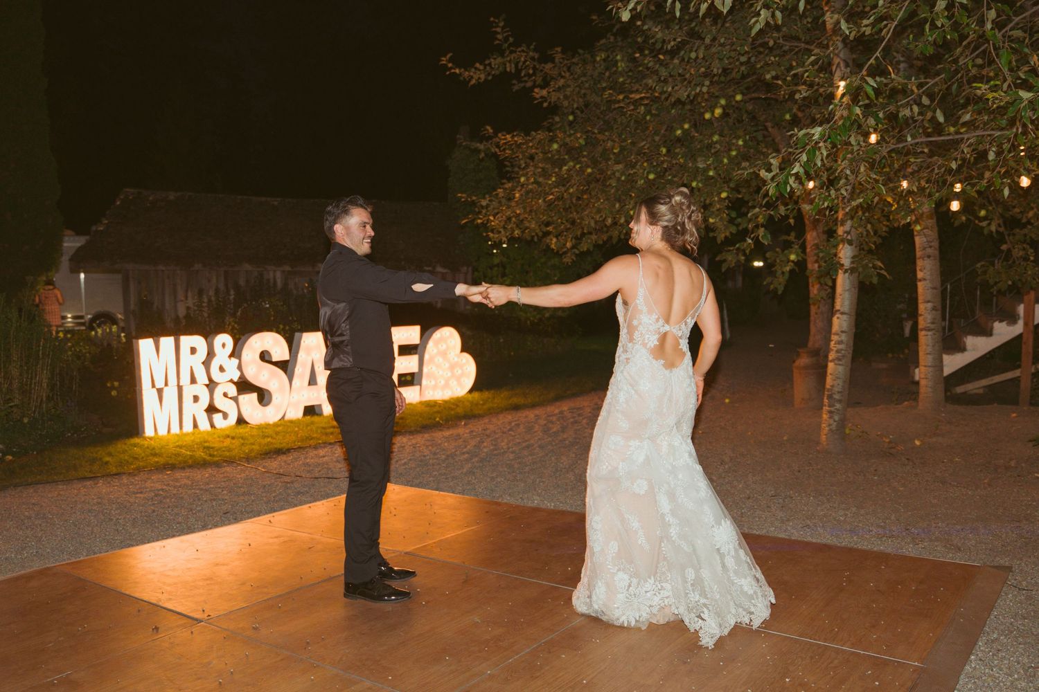 Outdoor wedding dance floor with illuminated 'MR&SAGE' sign glowing in the background.