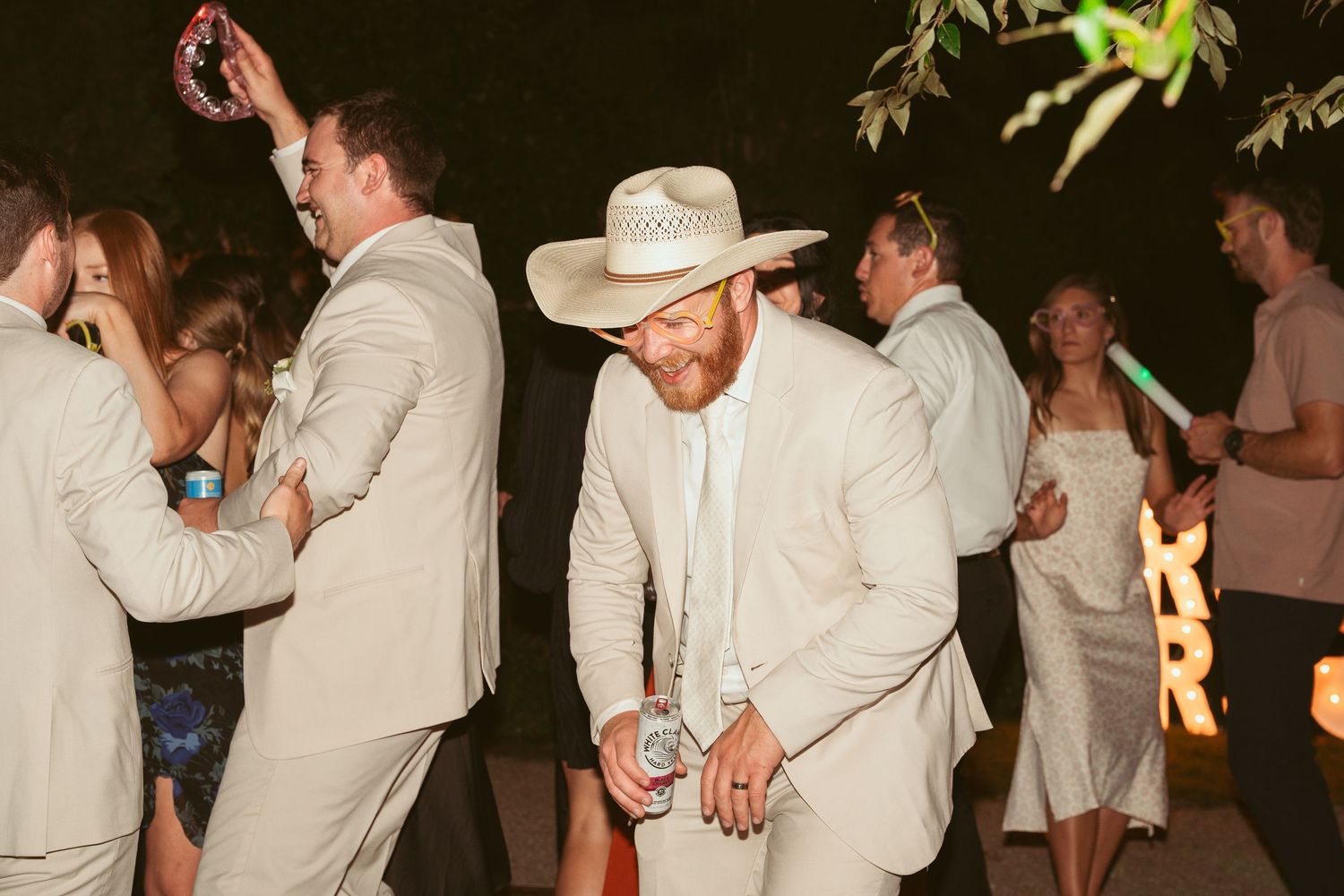 Wedding party dances together at an outdoor evening celebration with string lights.