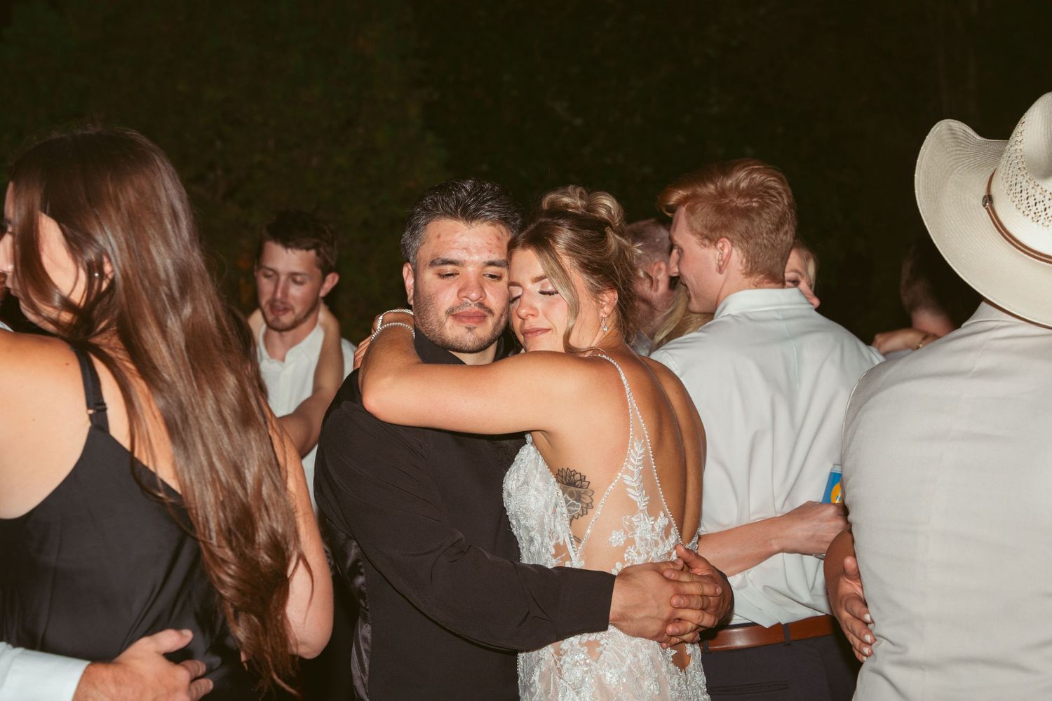 People dancing and embracing at a lively party or celebration in a dark room.