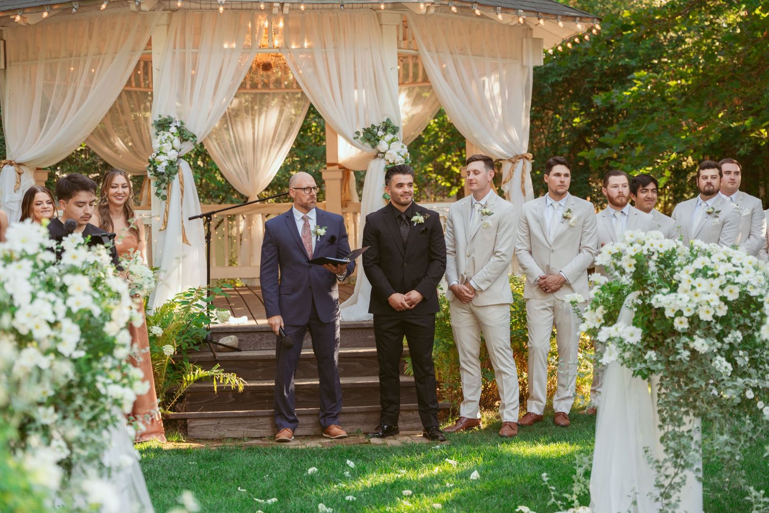 Elegant outdoor wedding ceremony setup with white draped gazebo and floral arrangements.