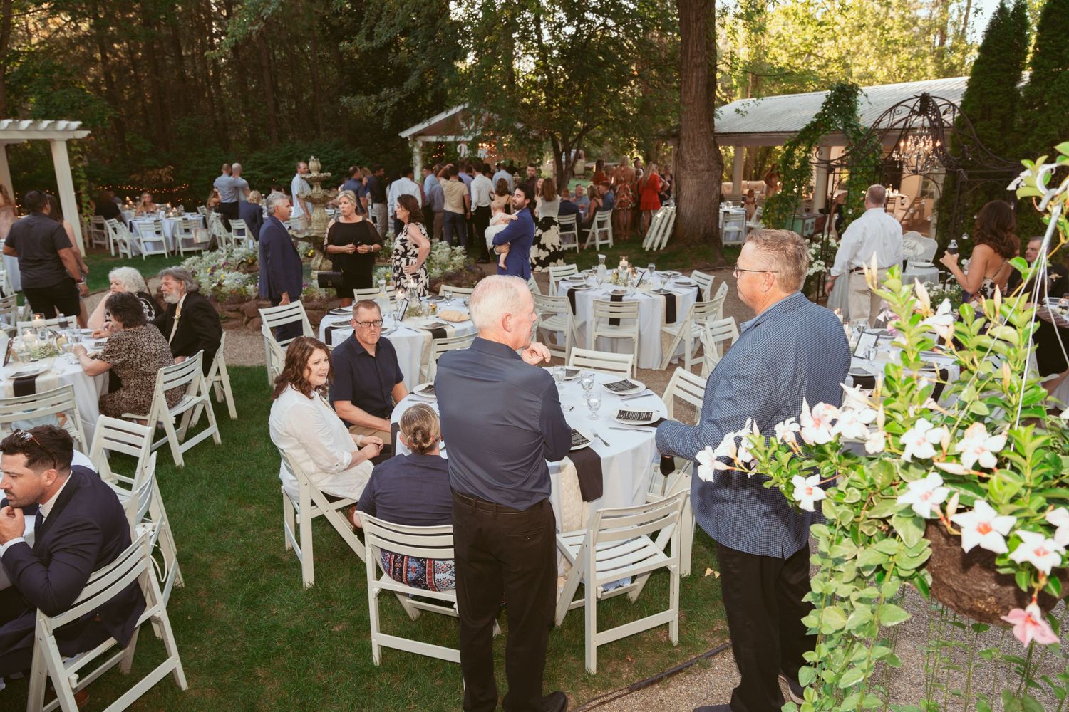 Garden wedding reception with white chairs arranged under trees at sunset.
