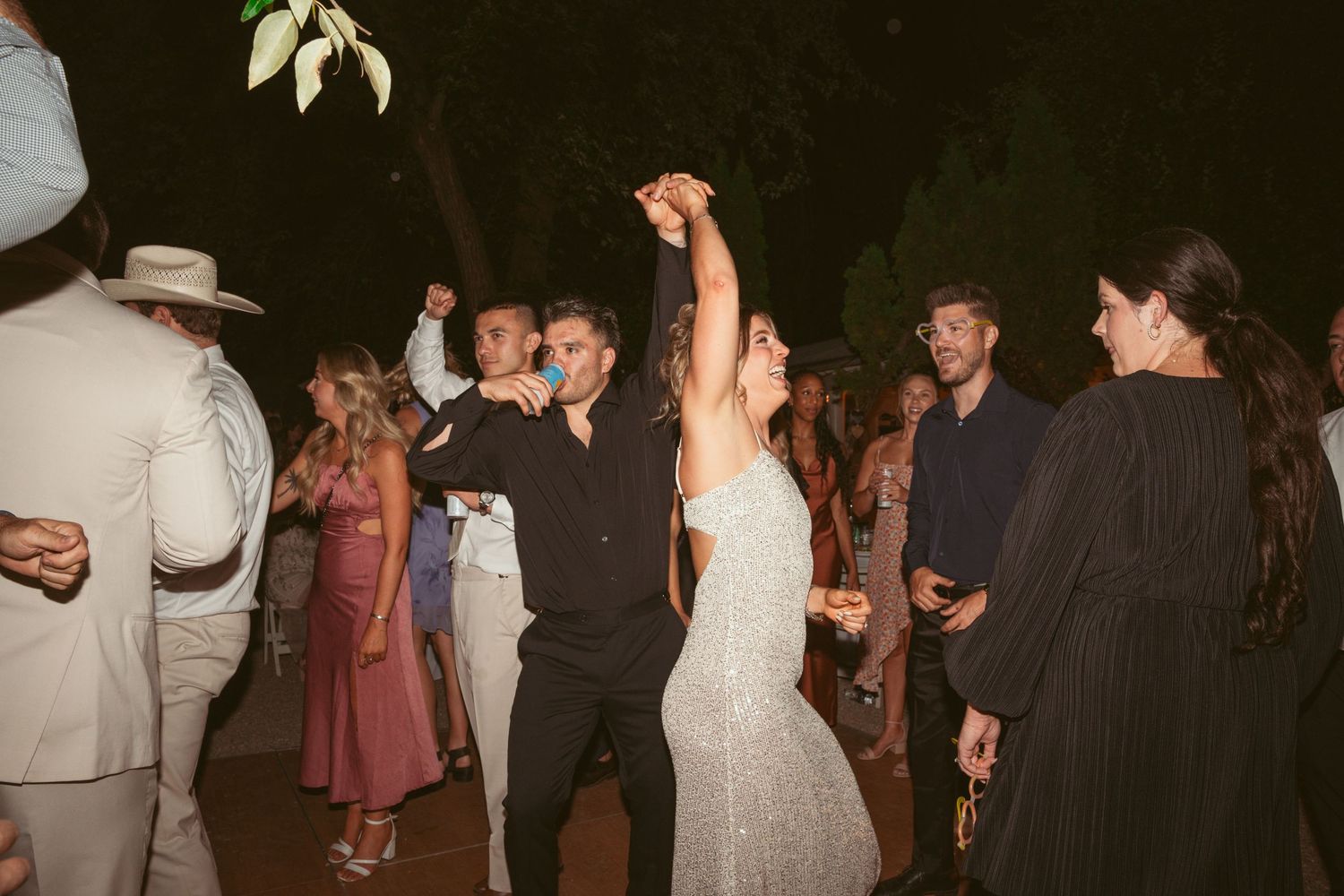 Wedding reception dance party with guests celebrating under outdoor lighting.