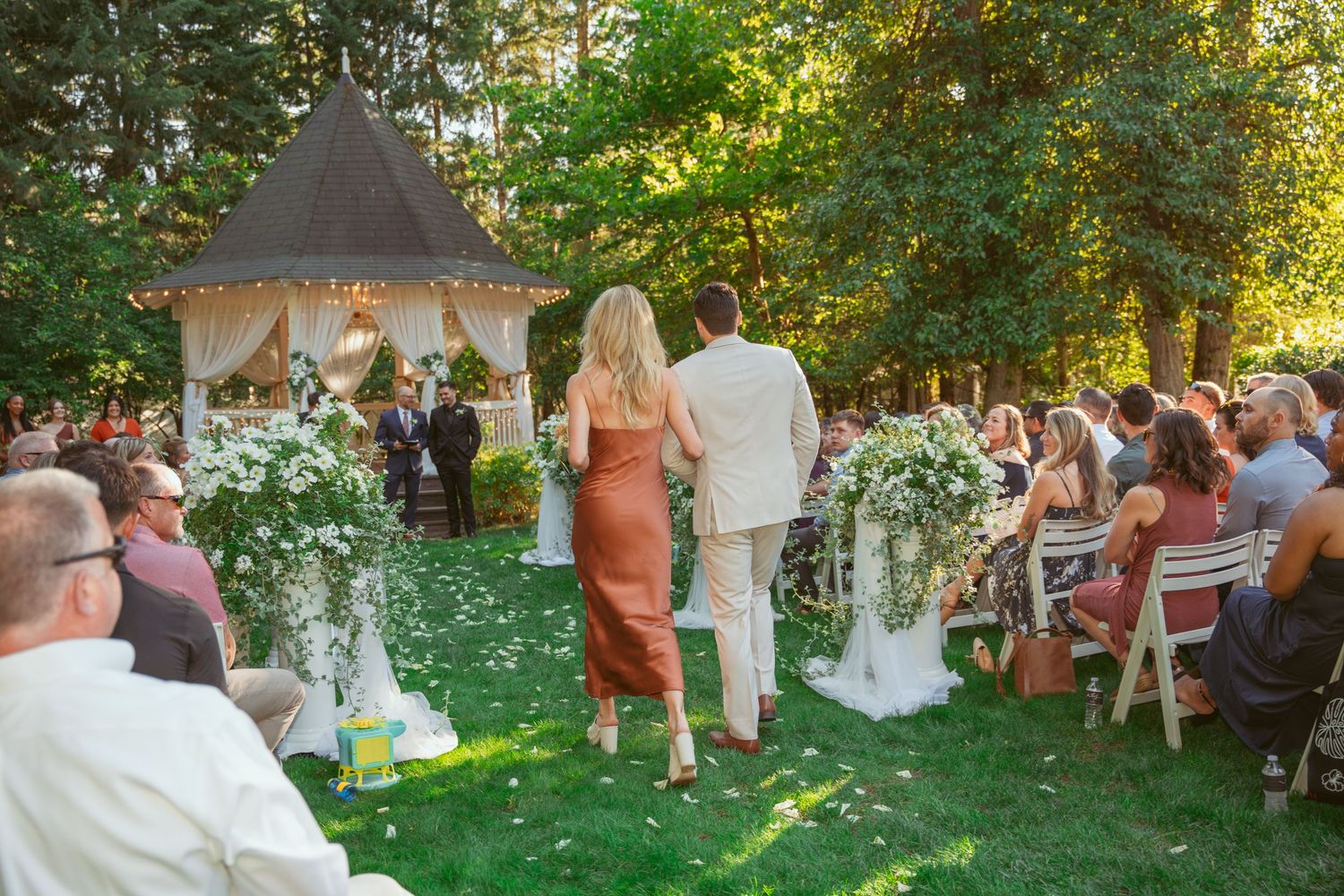 Outdoor wedding ceremony setup with white gazebo and rows of guest seating on grass.