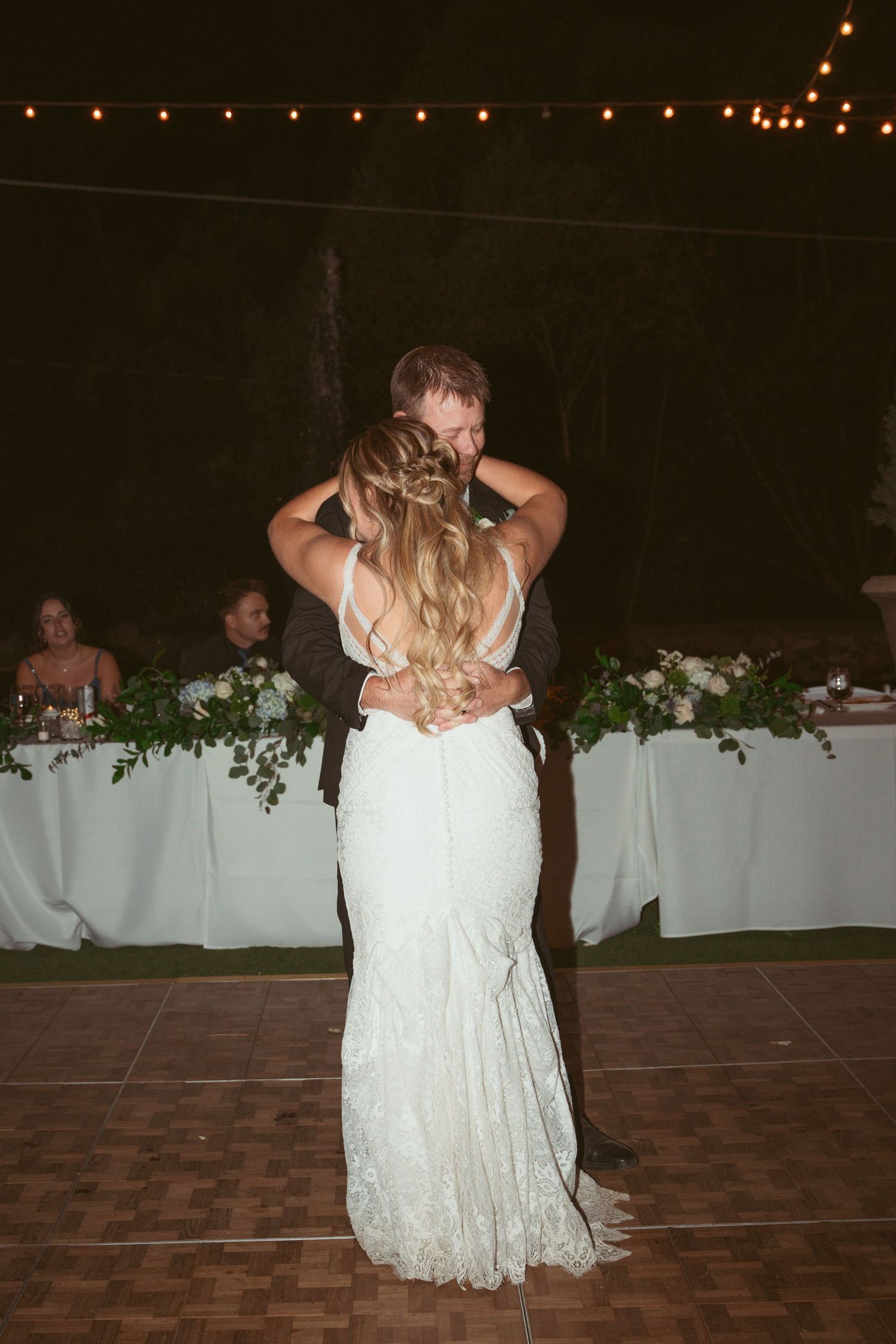 Wedding dance floor with string lights overhead and white floral decorations on tables.
