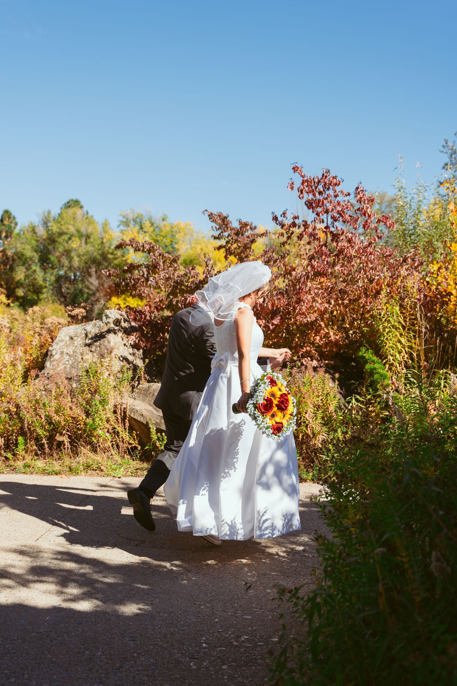 Wedding couple posing among colorful autumn foliage on an outdoor path.