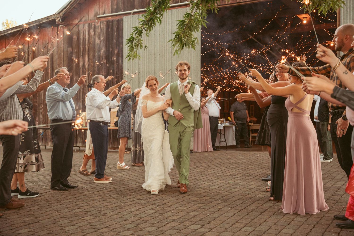 Guests create glowing sparkler arch for couple's grand exit at rustic outdoor wedding venue.