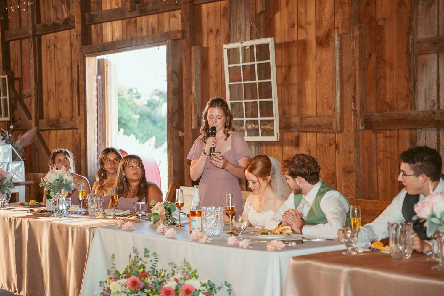 Panoramic view of wedding reception in rustic barn with natural light streaming through windows.