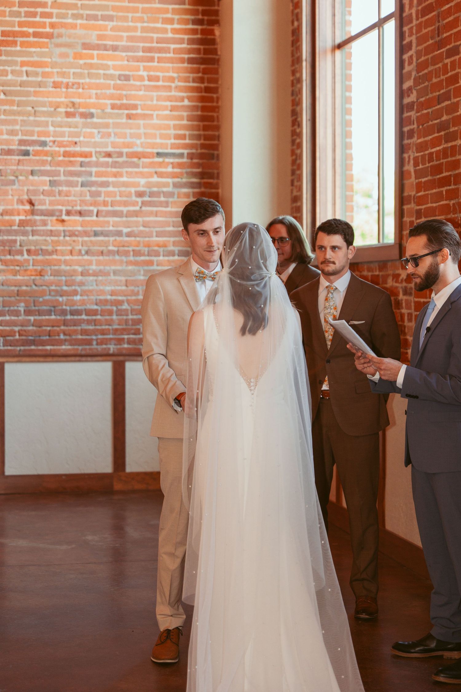 Wedding ceremony moments captured in a historic brick venue with large windows.