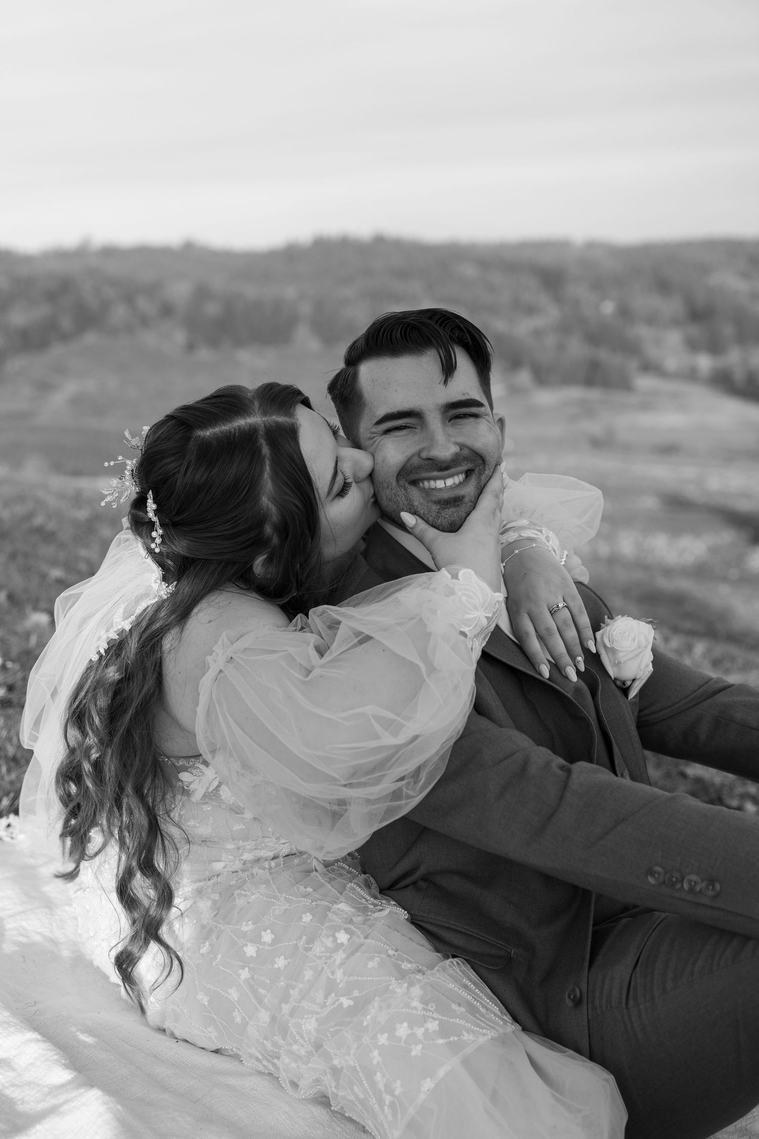 Couple in wedding attire embracing on a hilltop during golden hour.